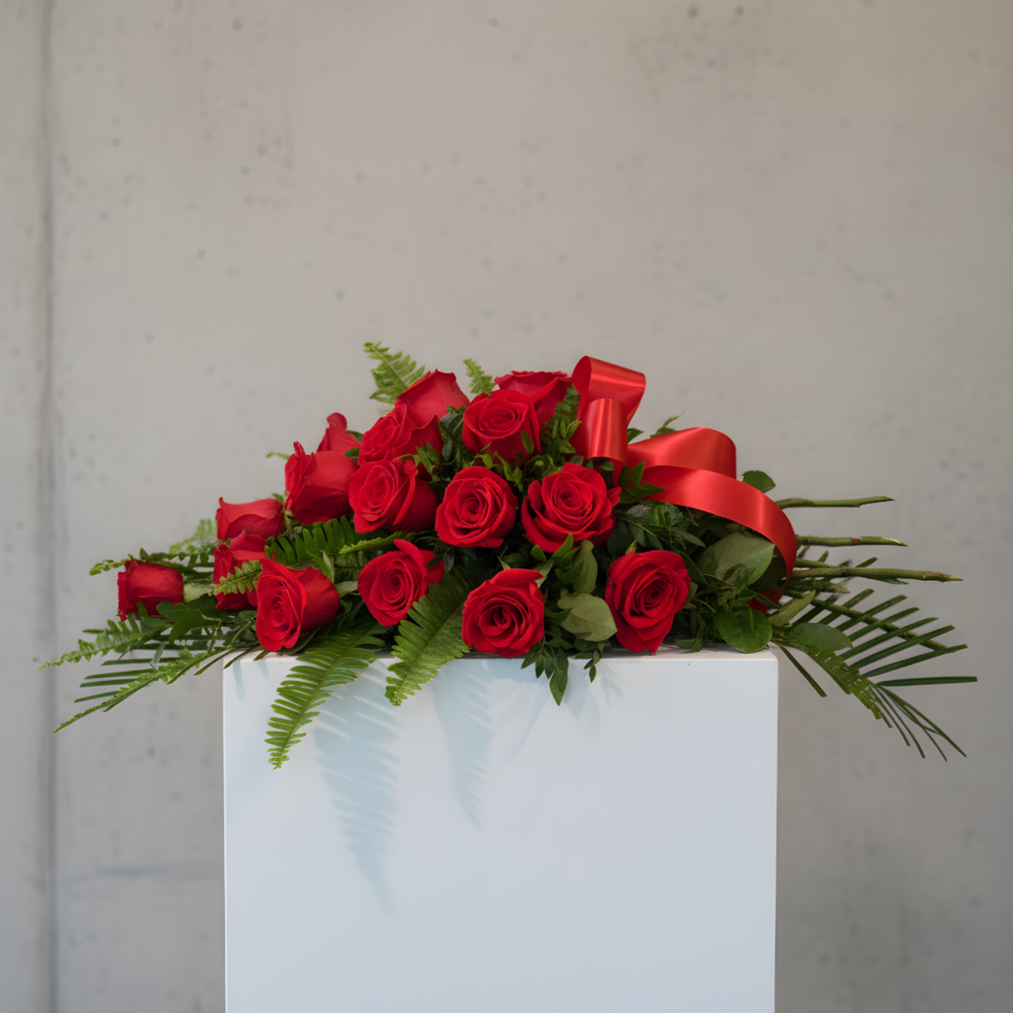 Red rose arrangement with a red ribbon on a white pedestal