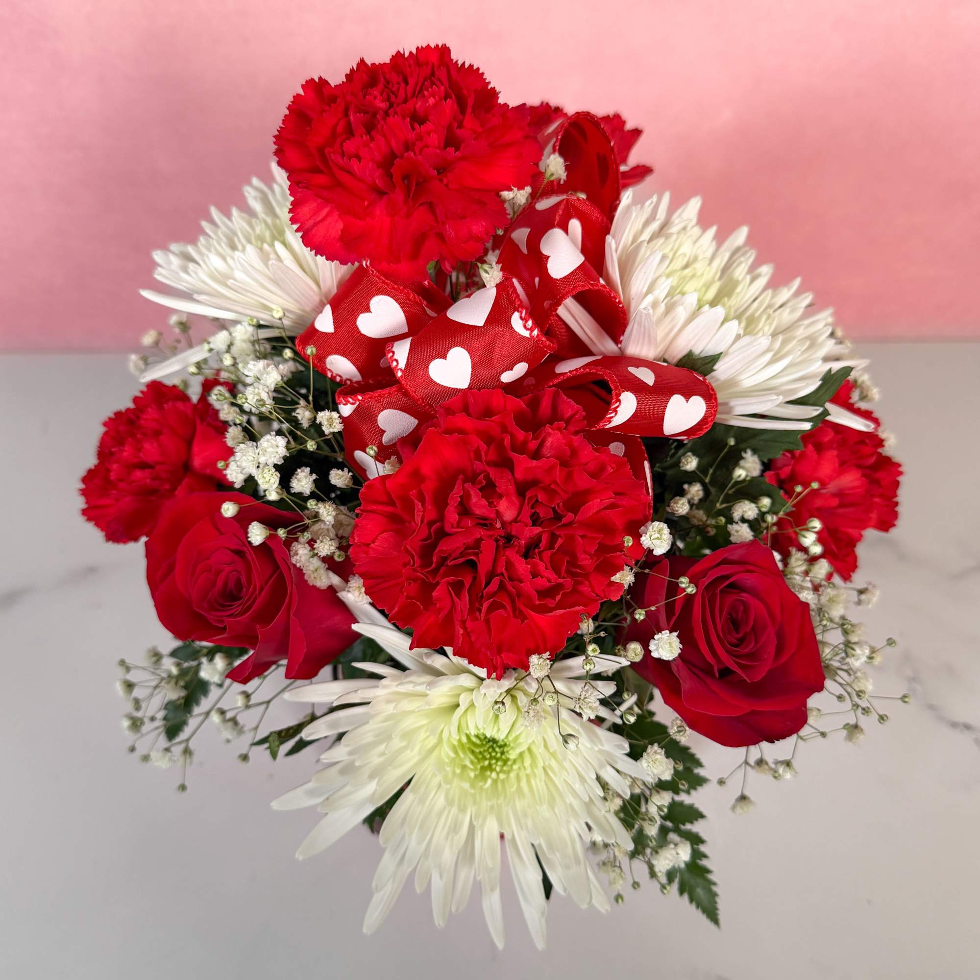 Red carnations and roses with white daisies and a heart ribbon