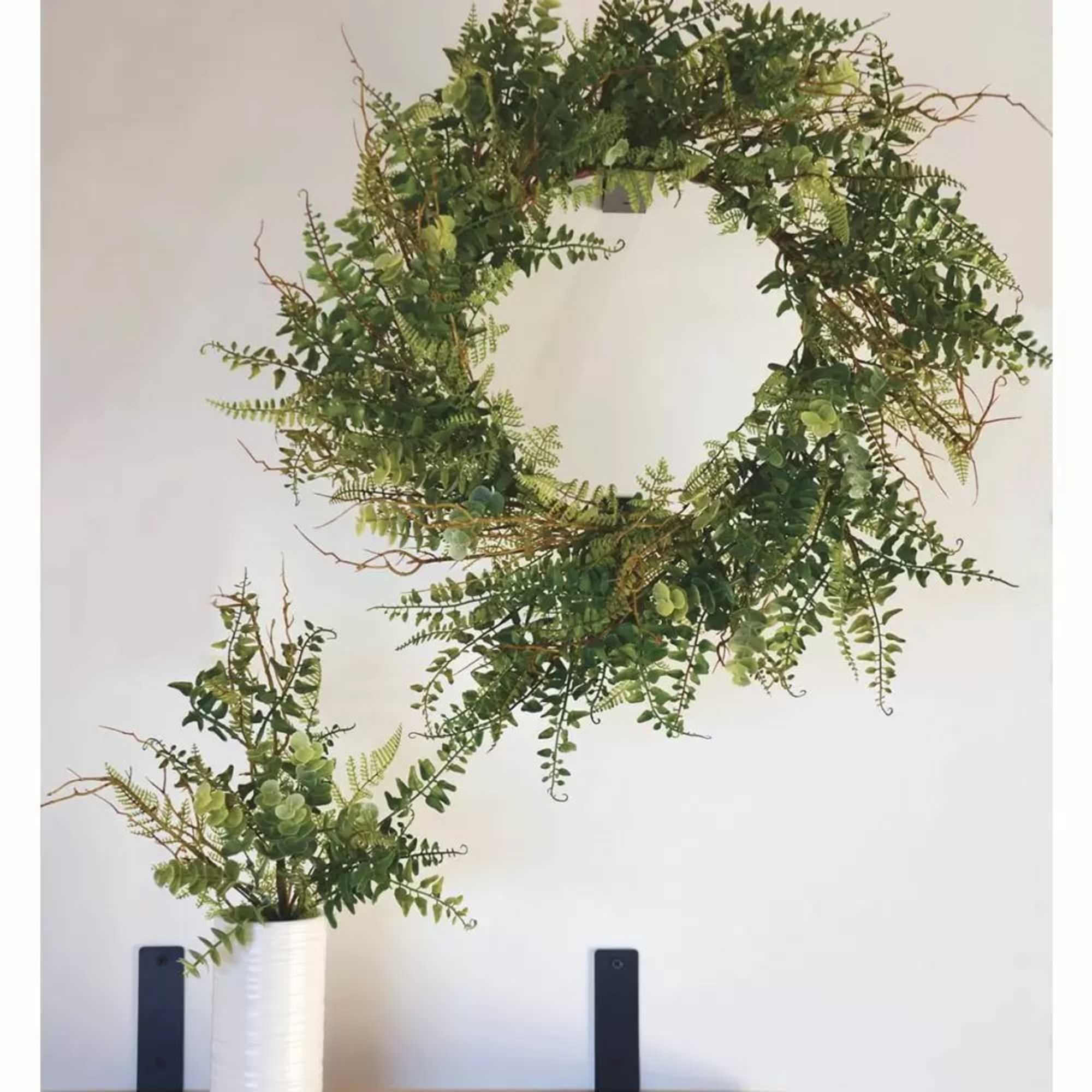 Green foliage wreath above a white vase arrangement