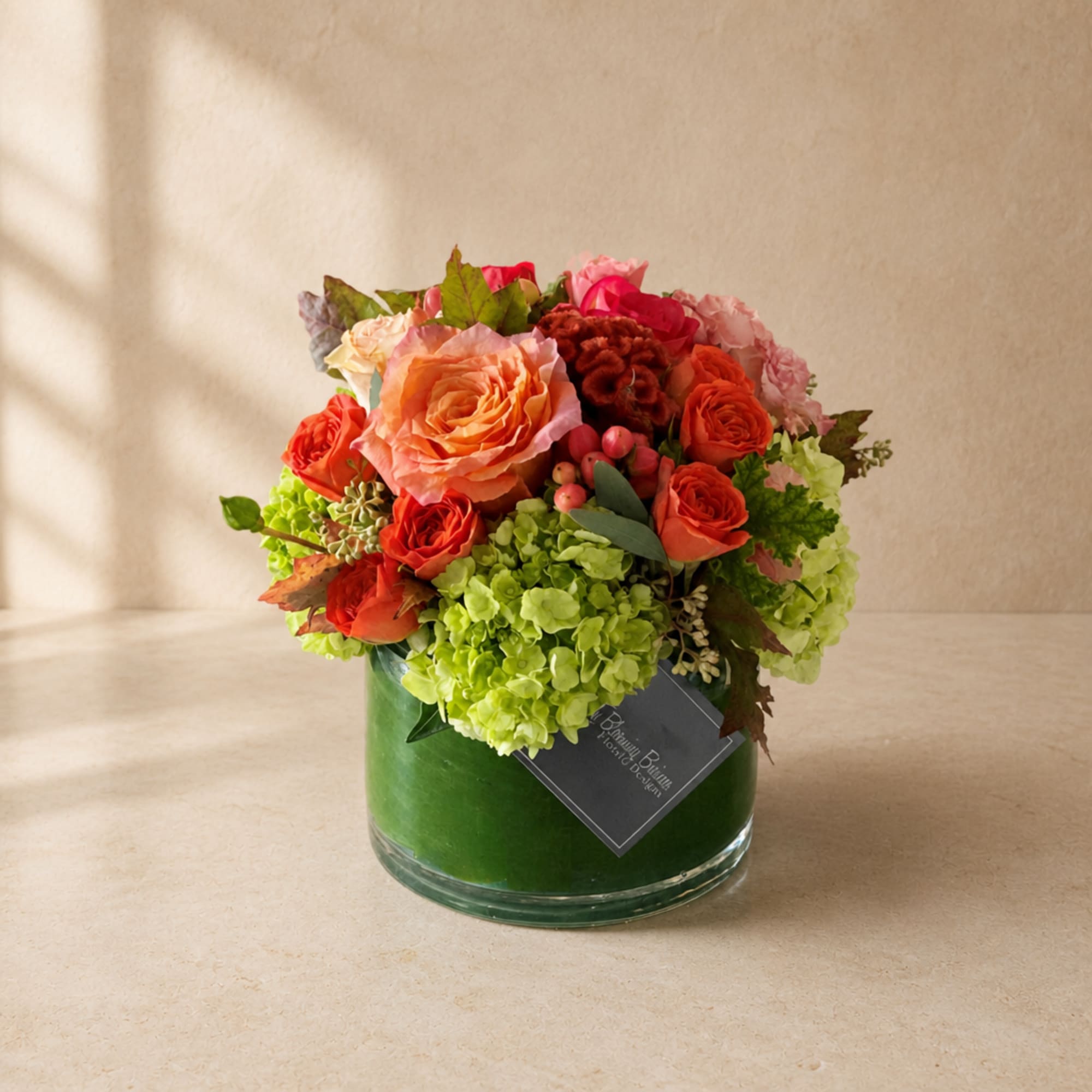 Mixed bouquet of orange and pink roses in a green glass vase