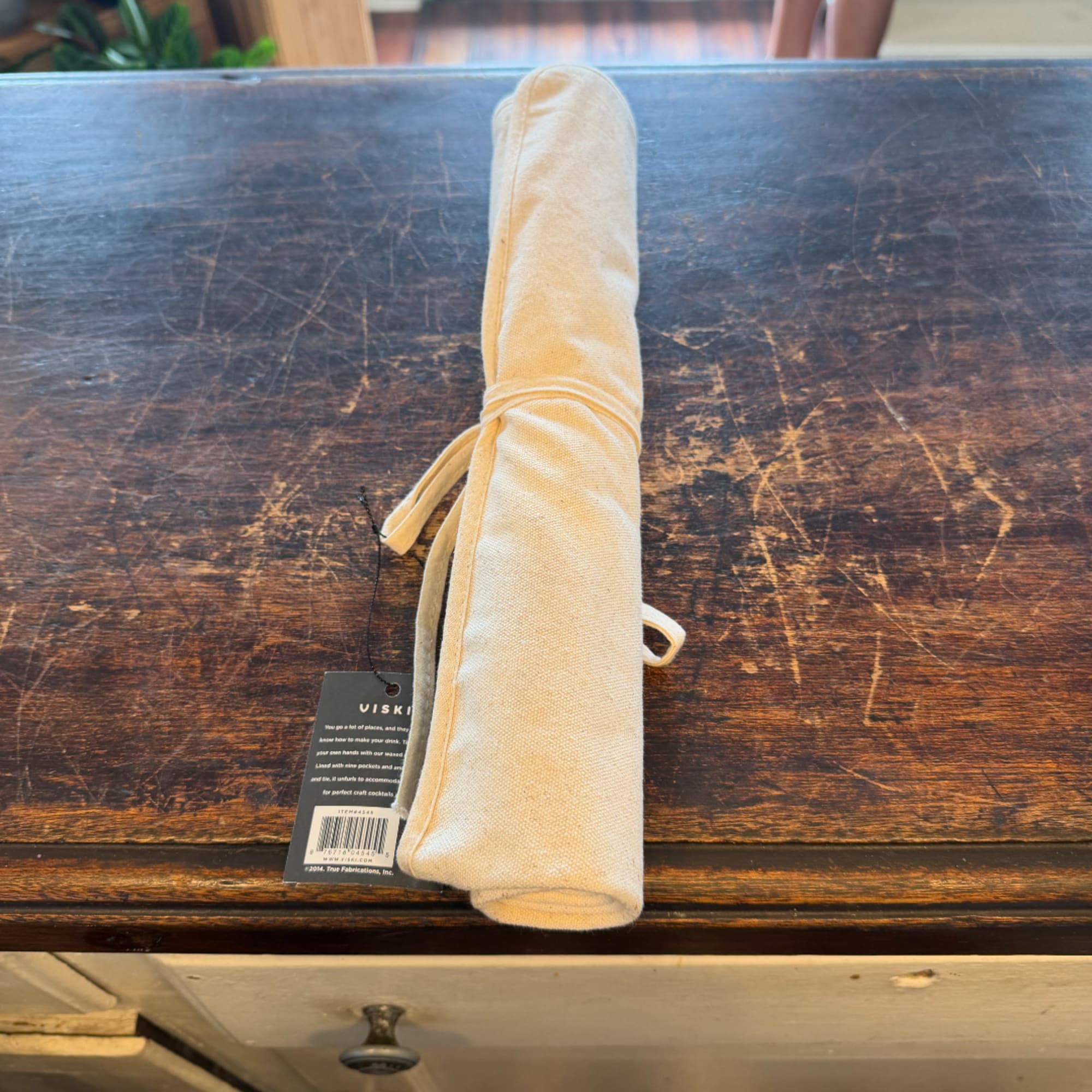 Rolled beige fabric item with a hanging tag on a wooden surface