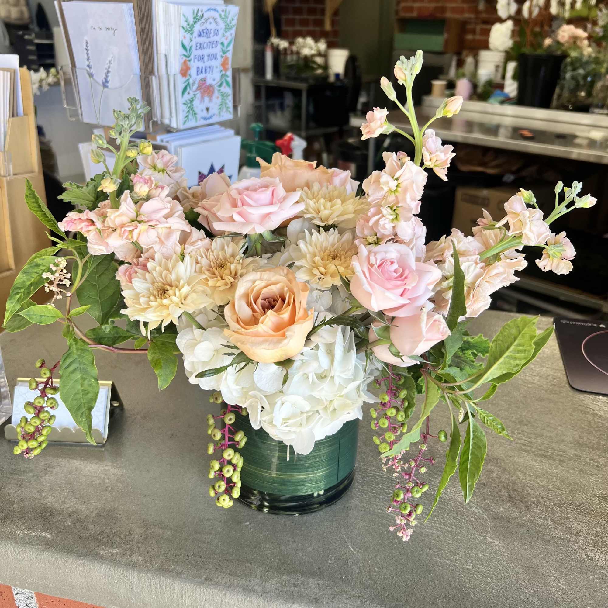 Pastel floral arrangement in a green glass vase with roses and hydrangea