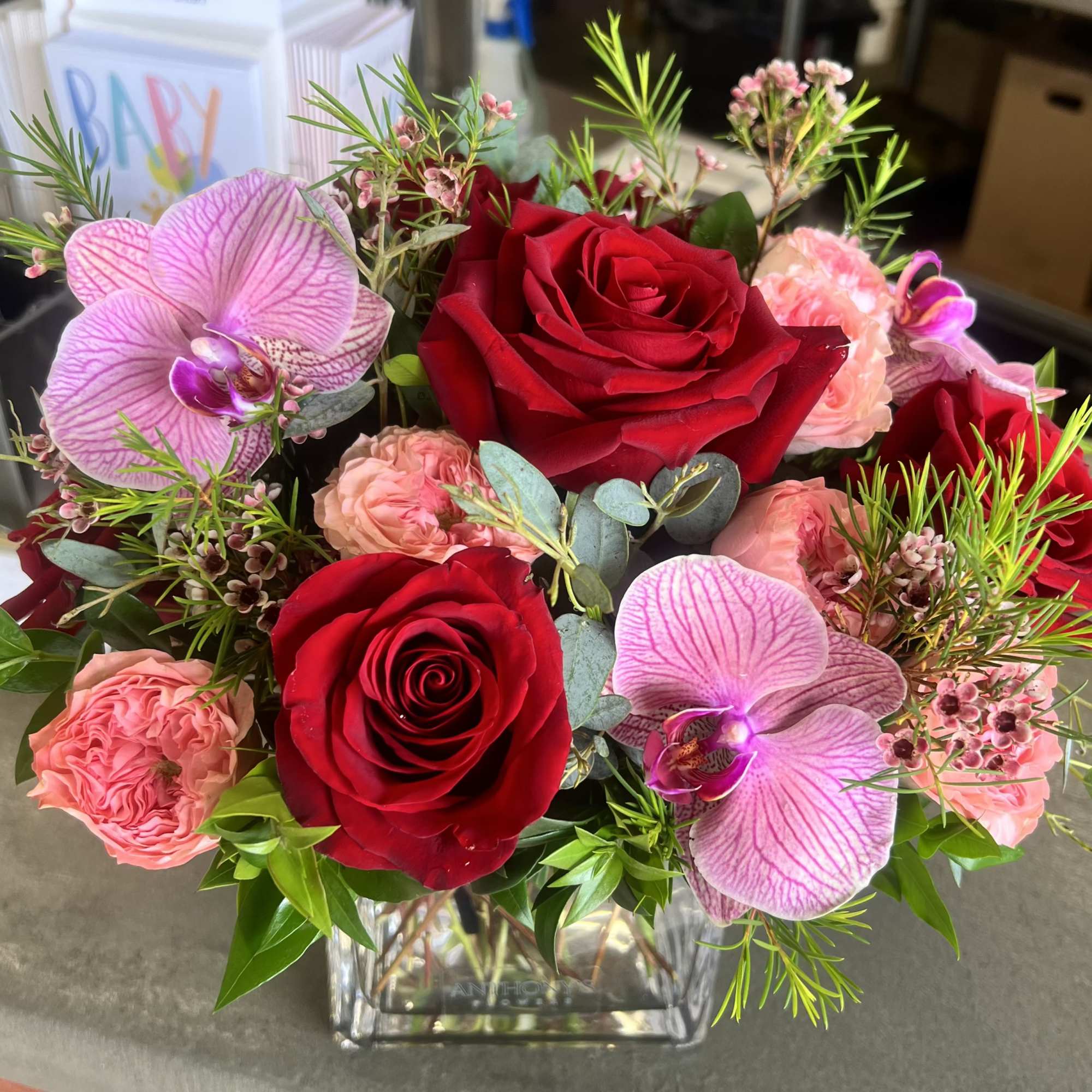 Red roses and pink orchids arranged in a clear square vase