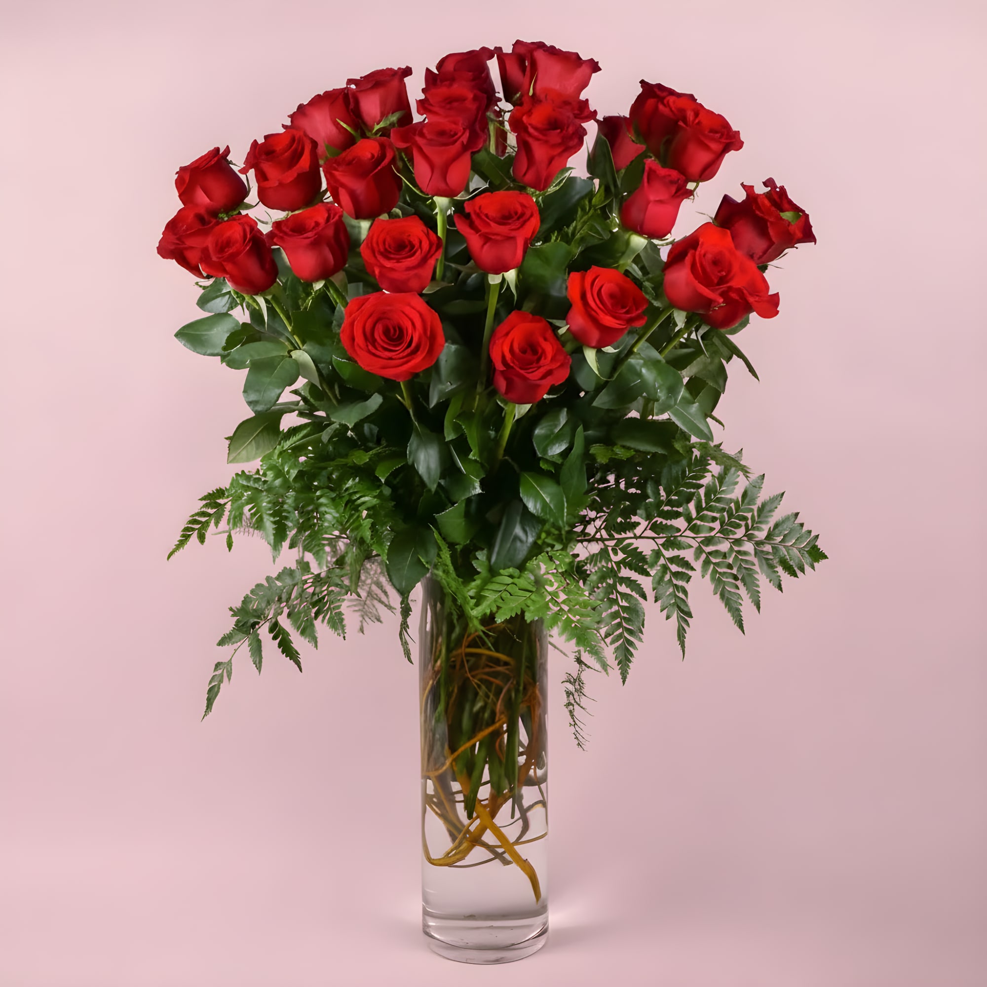 Red roses arranged in a tall clear glass vase with fern accents