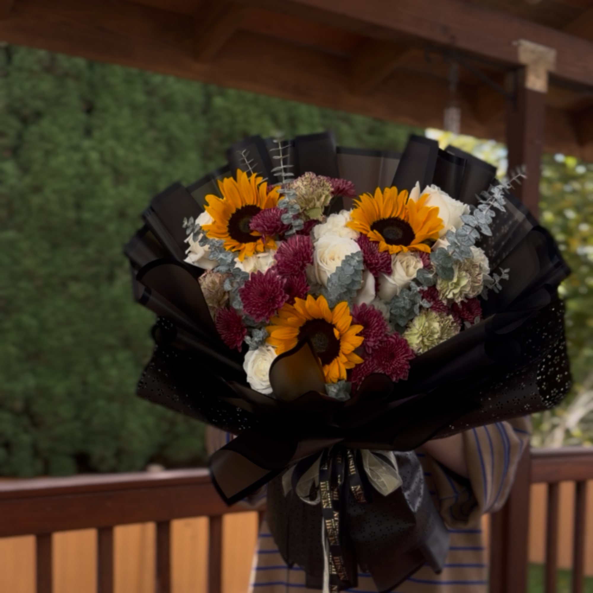 Bouquet of sunflowers, white roses, and burgundy mums wrapped in black paper