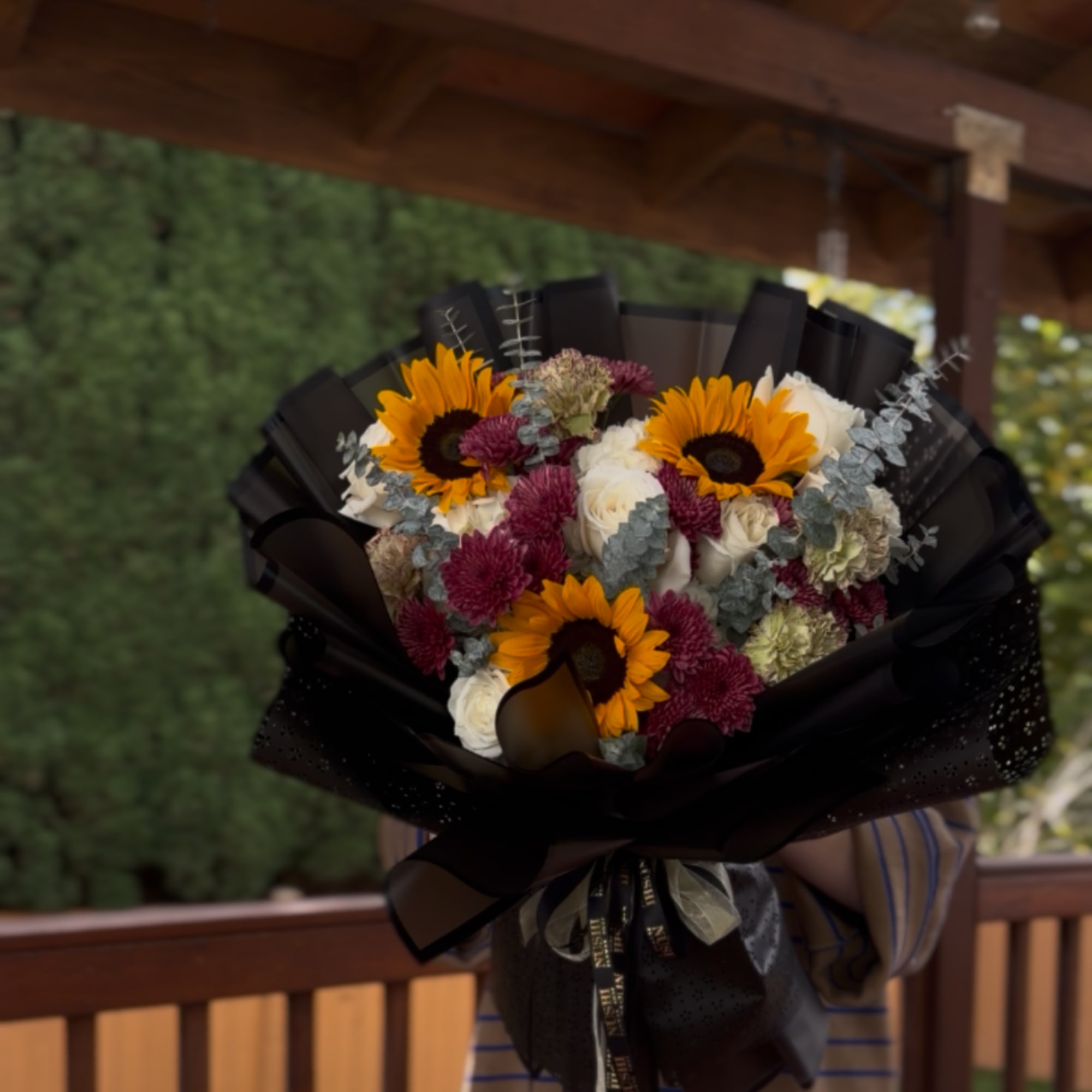 Bouquet of sunflowers, white roses, and burgundy flowers wrapped in black paper