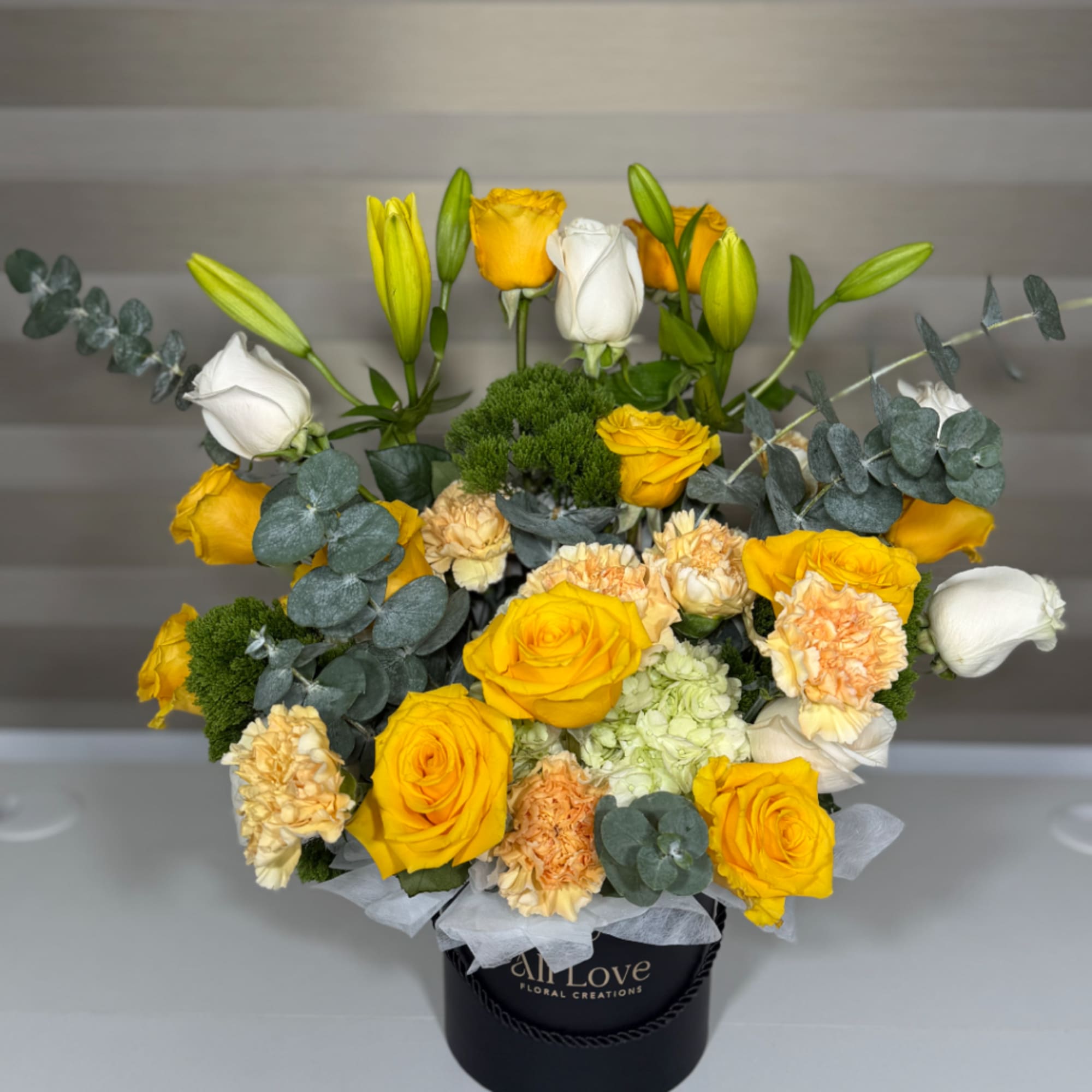 Yellow roses, white lilies, and carnations in a black hatbox
