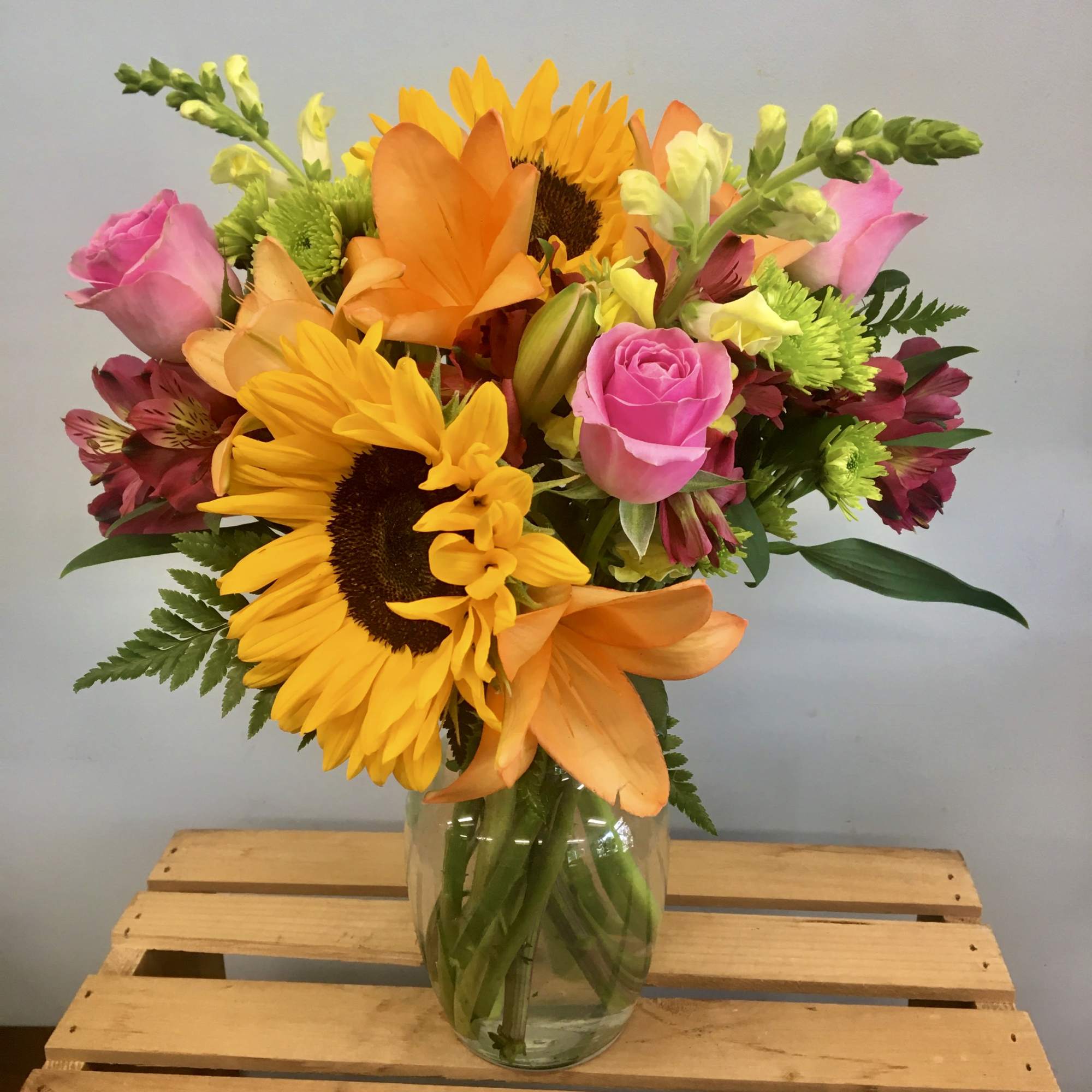 Mixed bouquet of sunflowers, pink roses, and orange lilies in a glass vase
