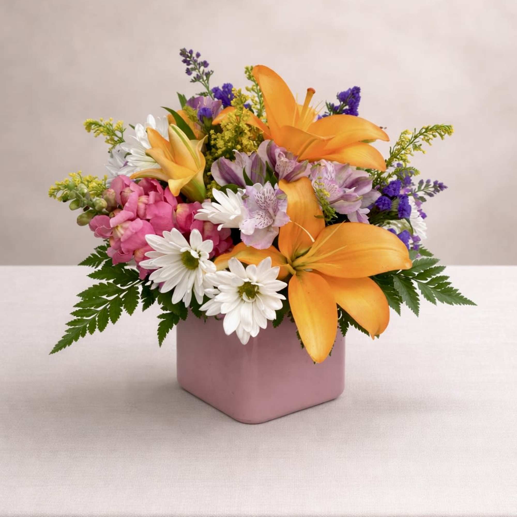 Mixed bouquet of orange lilies, pink flowers, and white daisies in a pink vase