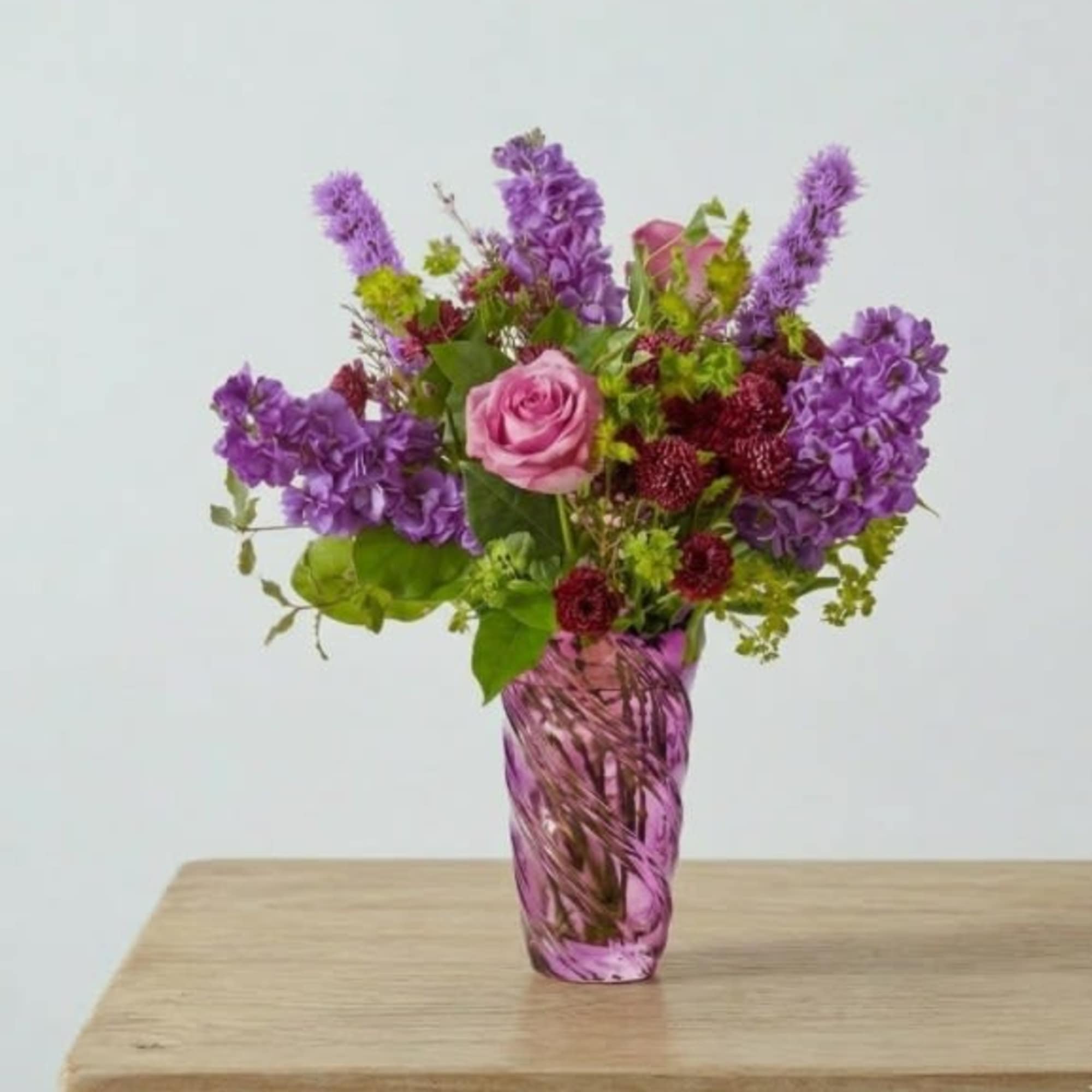 Pink and purple flower arrangement in a purple glass vase