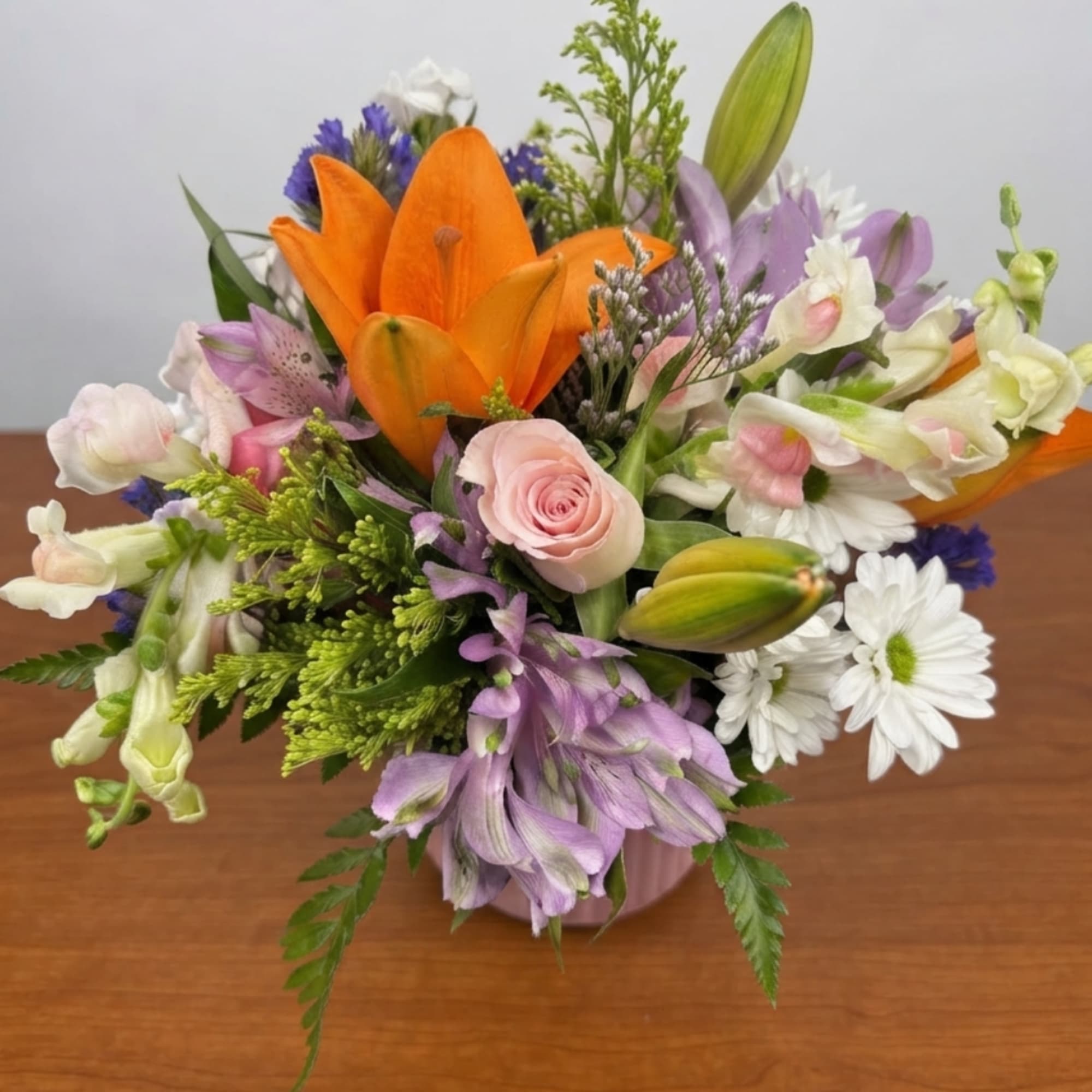Mixed bouquet with orange lilies, pink roses, and white daisies in a pink vase