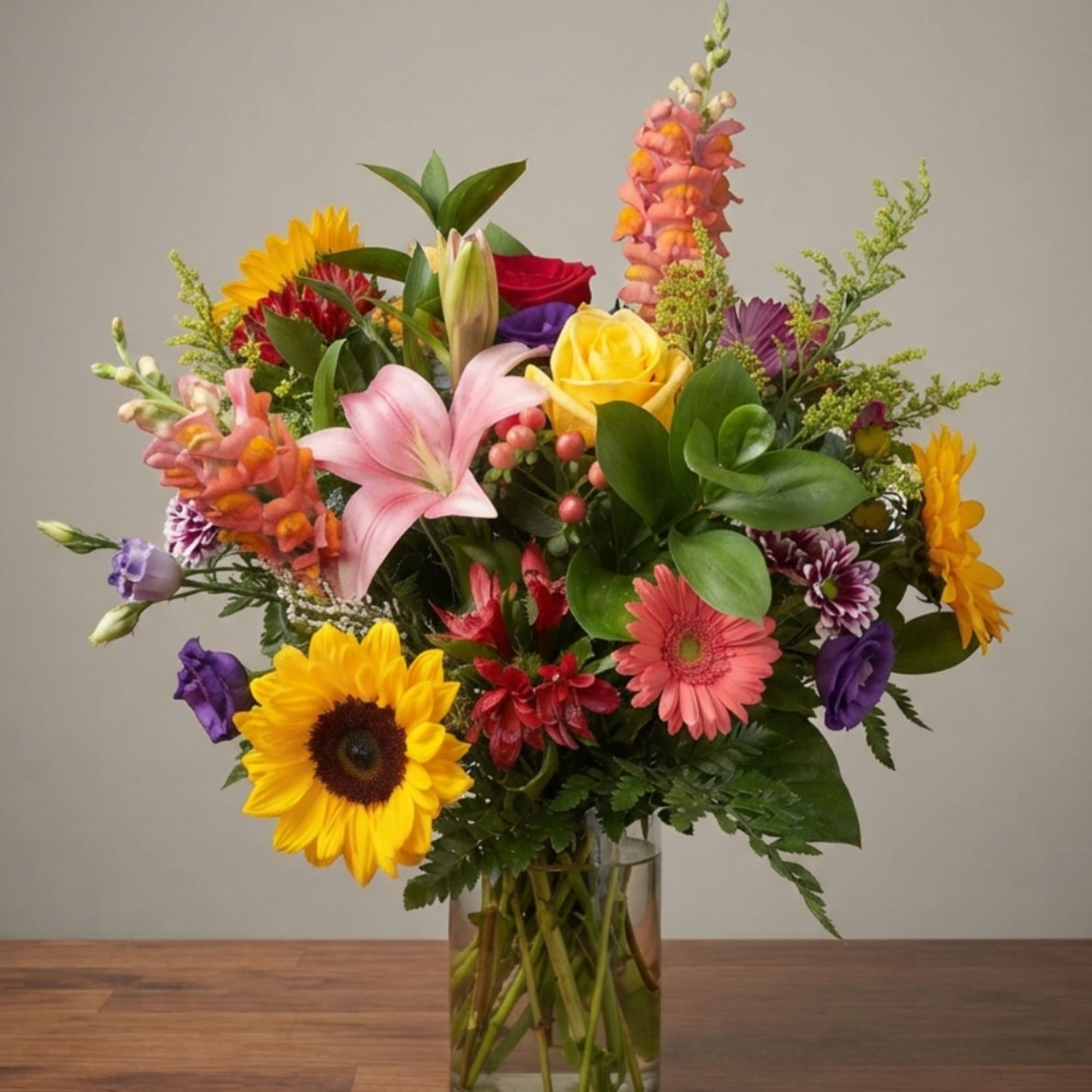 Mixed bouquet with sunflowers, lilies, roses, and gerbera daisies in a clear vase