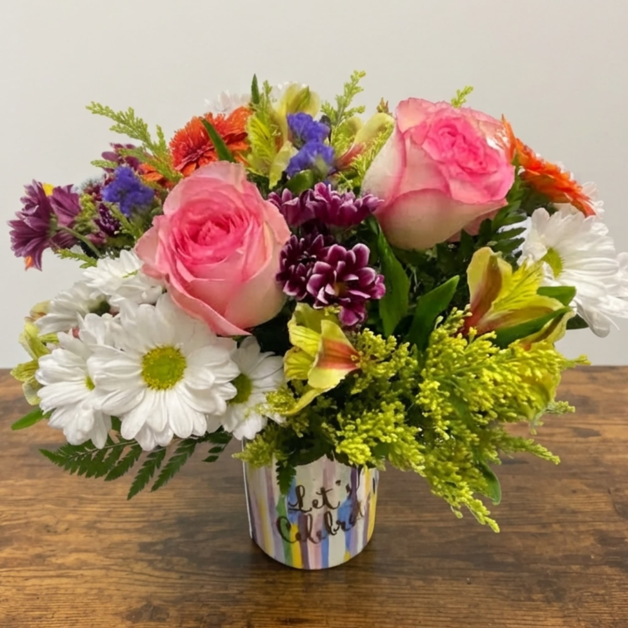 Mixed bouquet of pink roses, white daisies, and colorful flowers in a striped vase