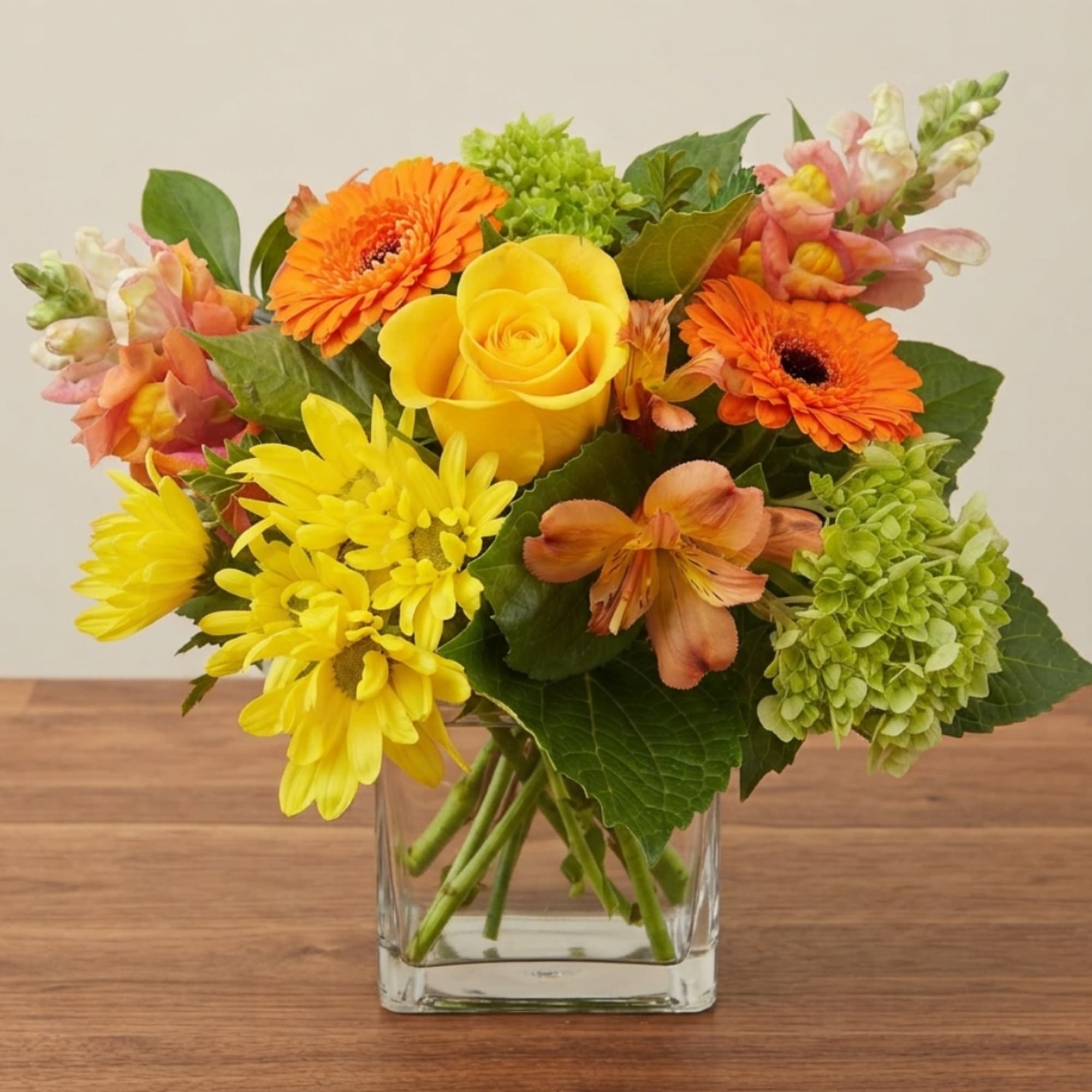 Mixed bouquet of yellow, orange, and pink flowers in a clear glass vase