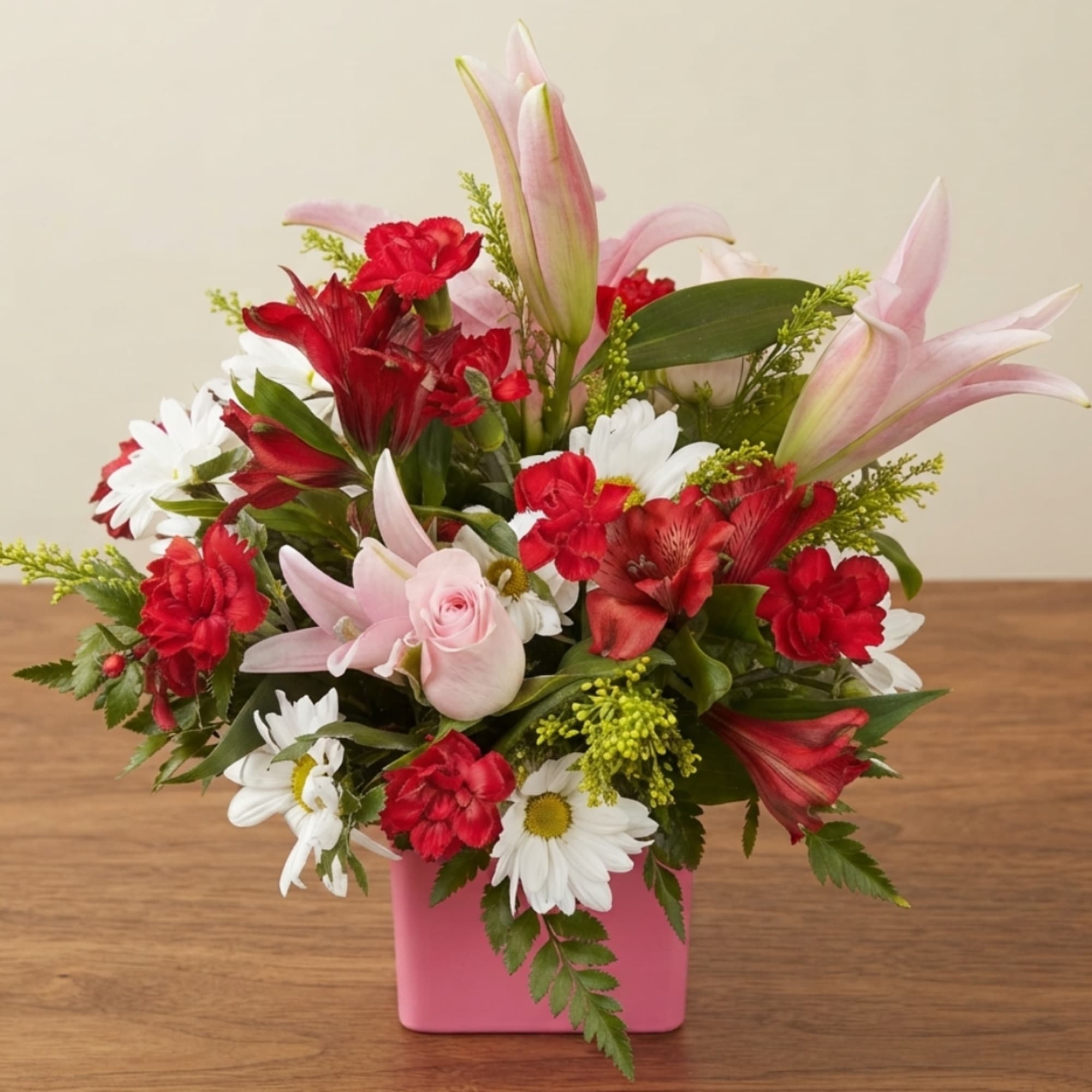 Pink lilies, red carnations, and white daisies in a pink vase