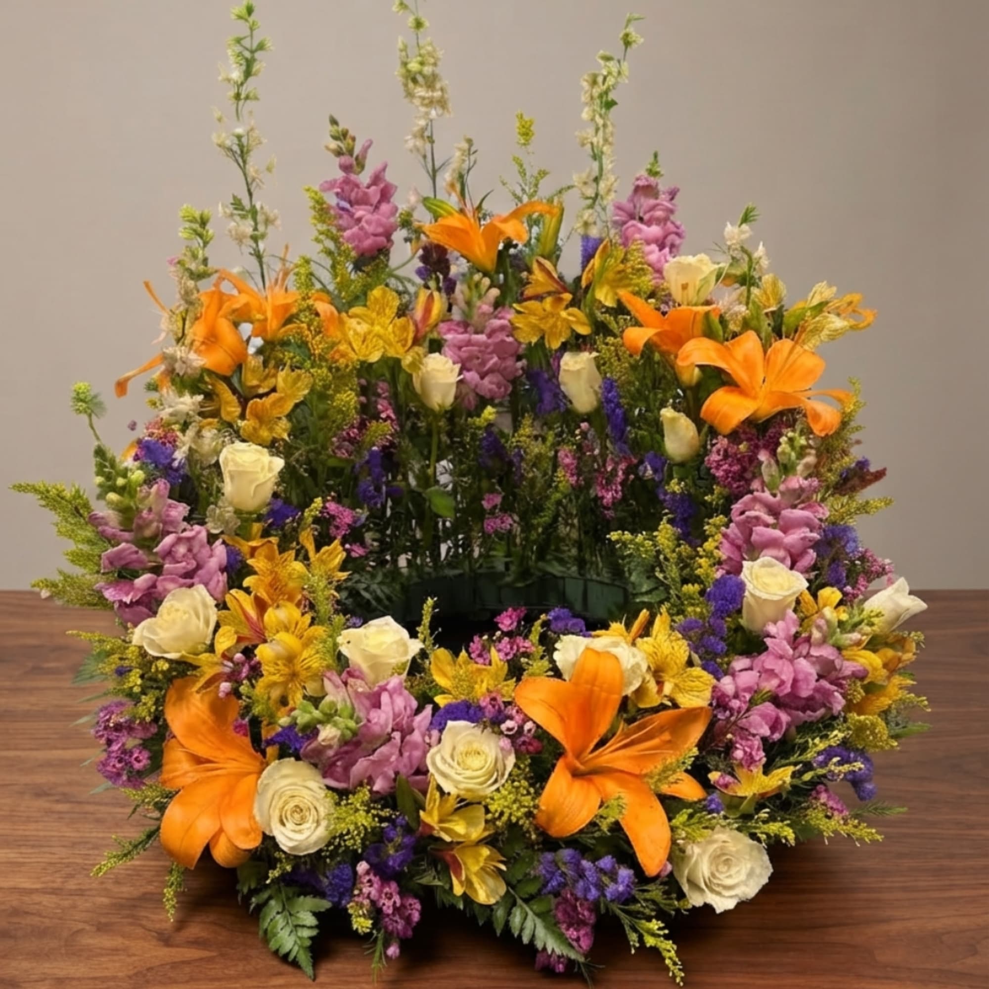 Large circular floral arrangement with orange lilies, cream roses, and purple blooms
