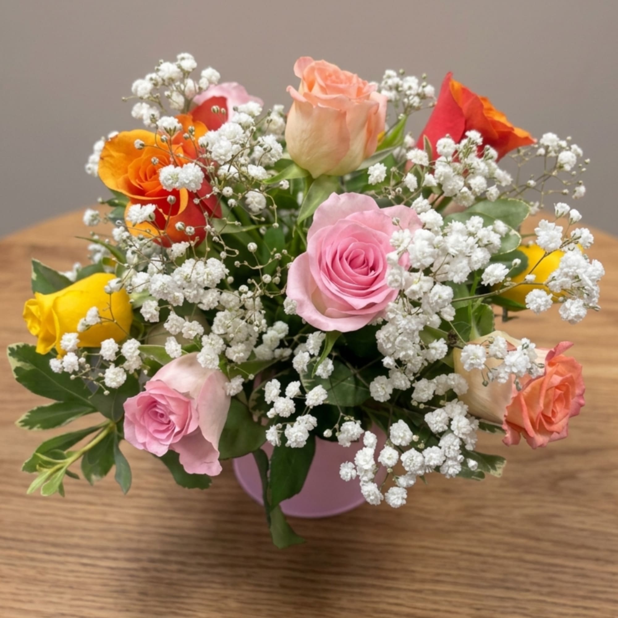 Mixed roses with baby's breath in a pink vase on a wooden table