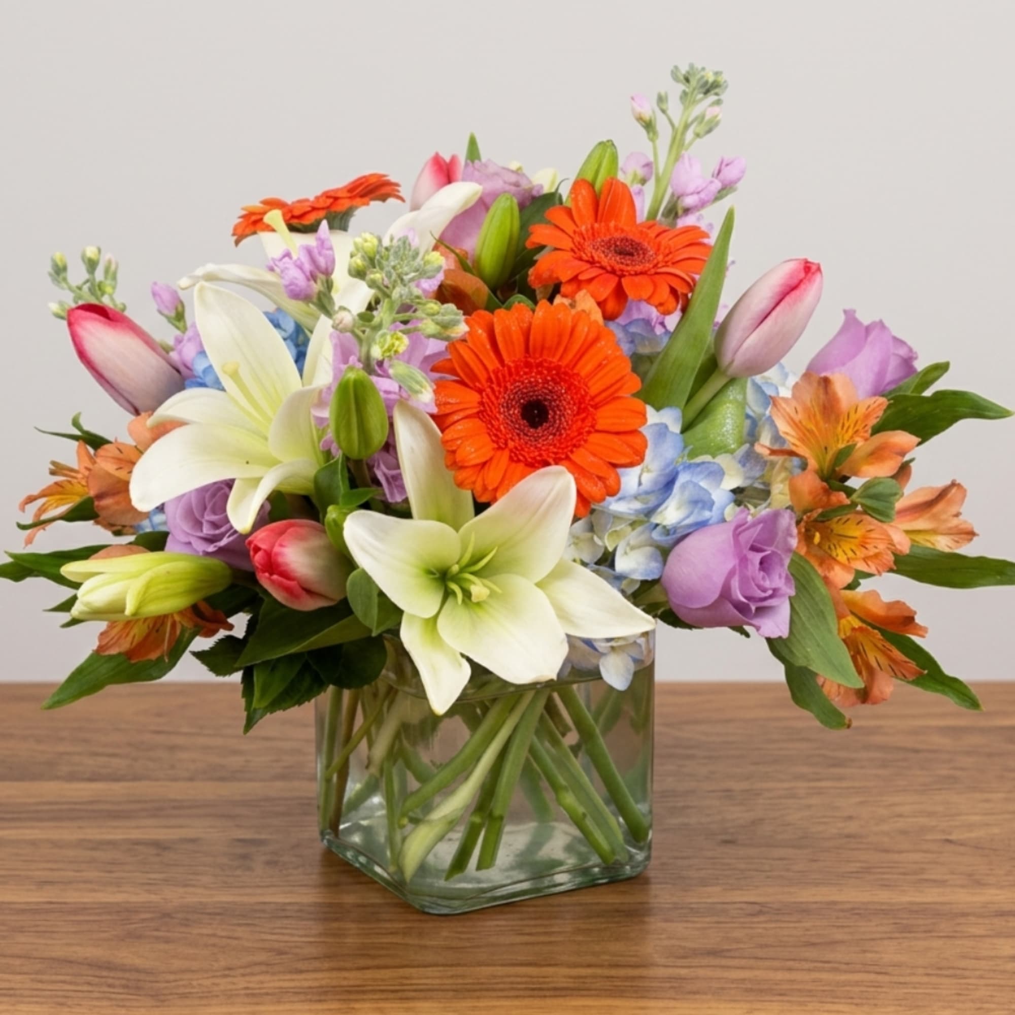 Mixed bouquet of lilies, gerbera daisies, tulips, and hydrangeas in a glass vase