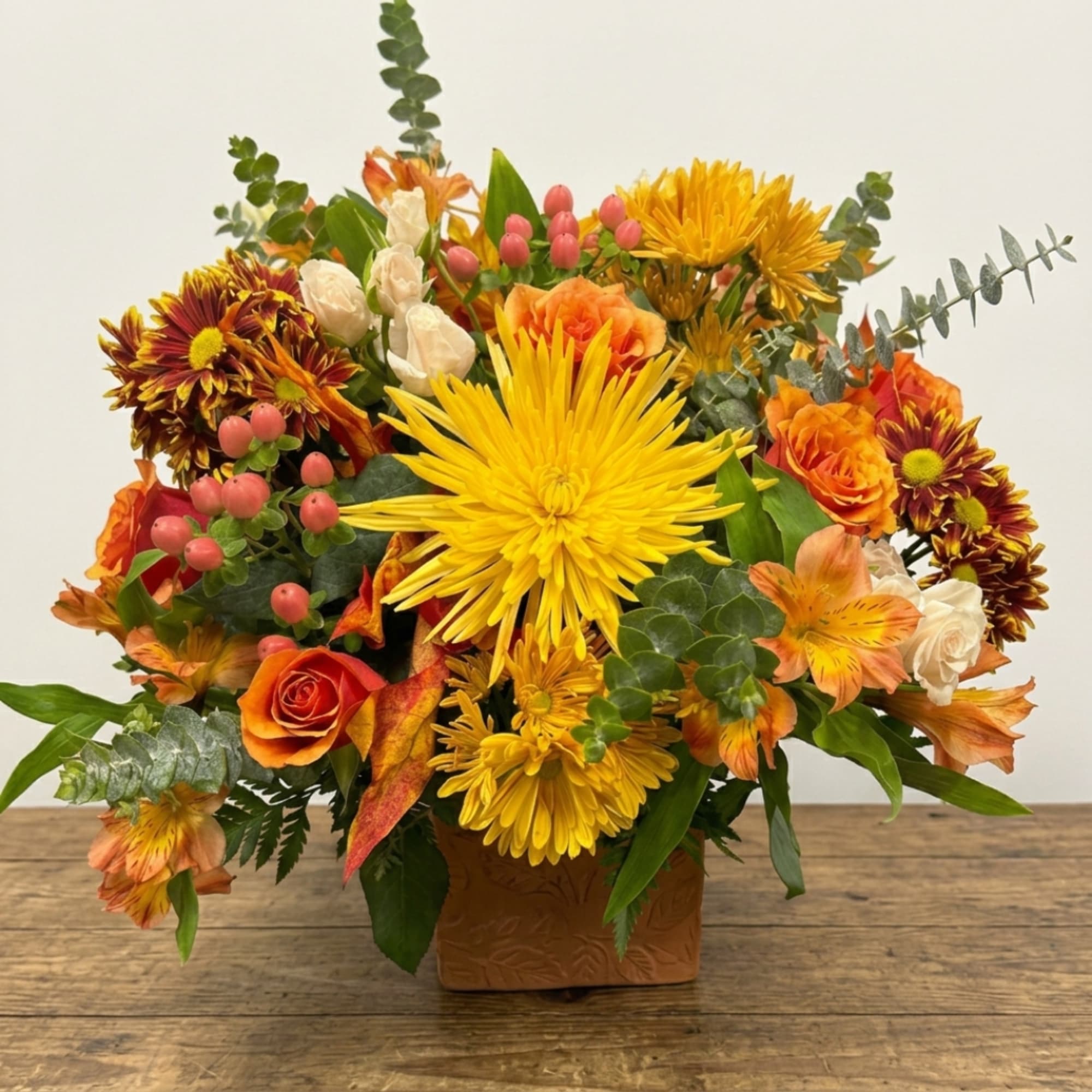 Autumn flower arrangement with yellow chrysanthemums and orange roses in a square vase
