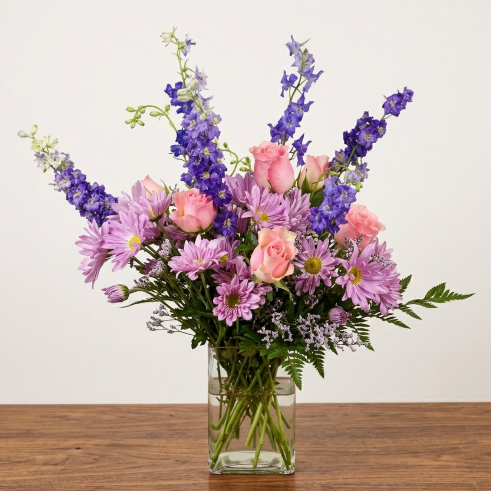 Pink roses and purple daisies in a clear glass vase