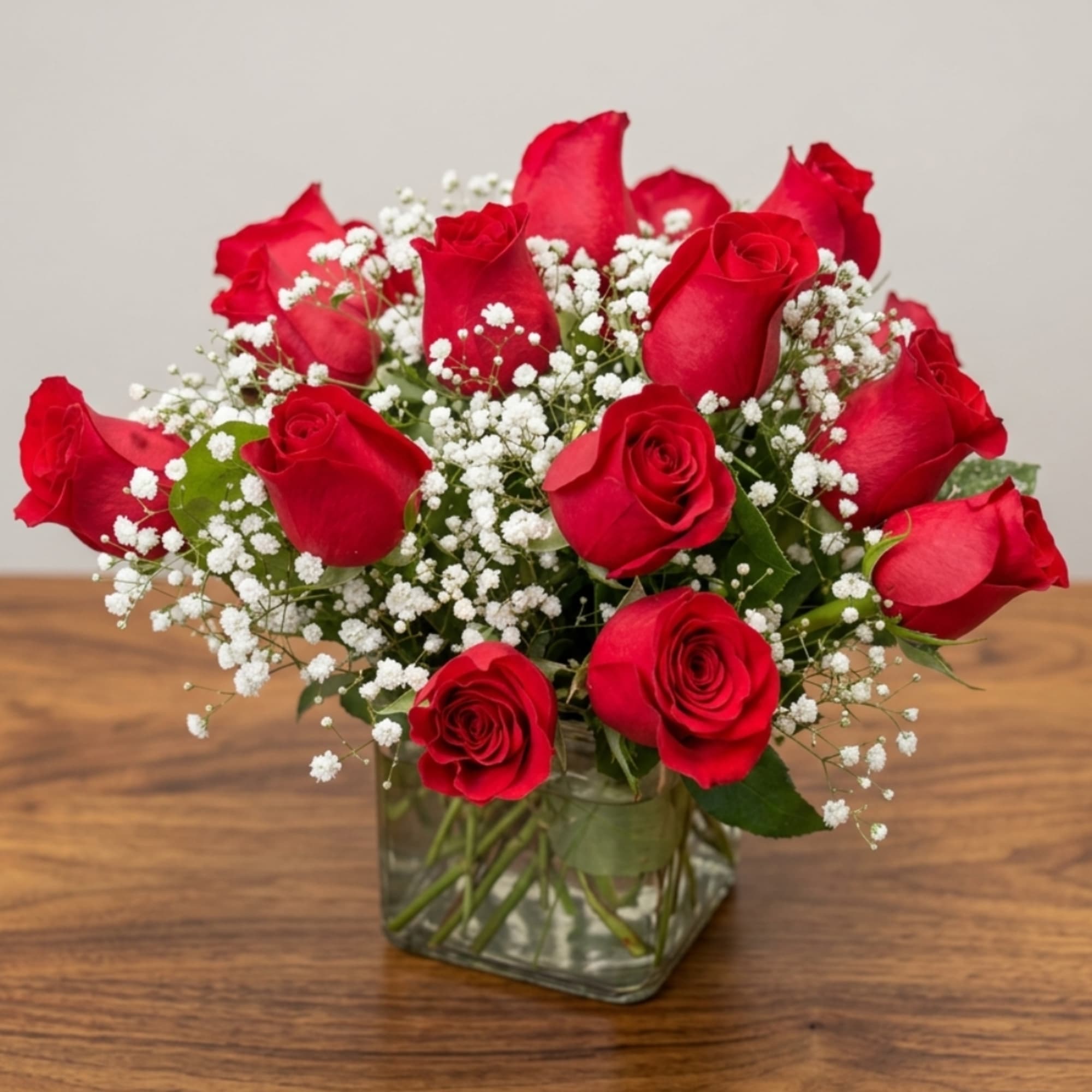 Red roses arranged in a clear glass vase with white baby's breath