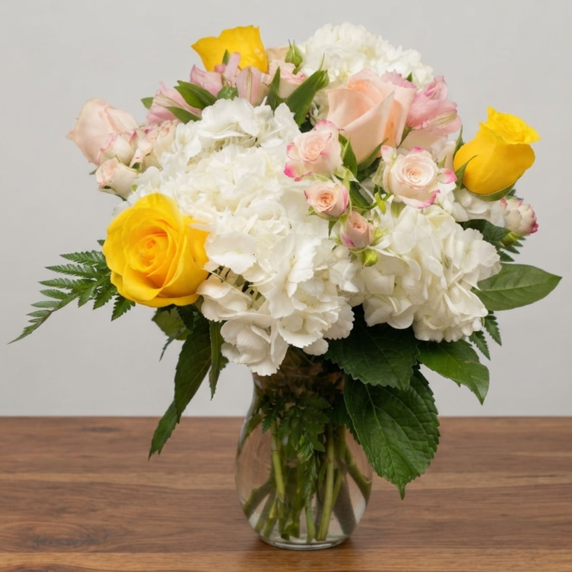 Bouquet of yellow and pale pink roses with white hydrangeas in a glass vase
