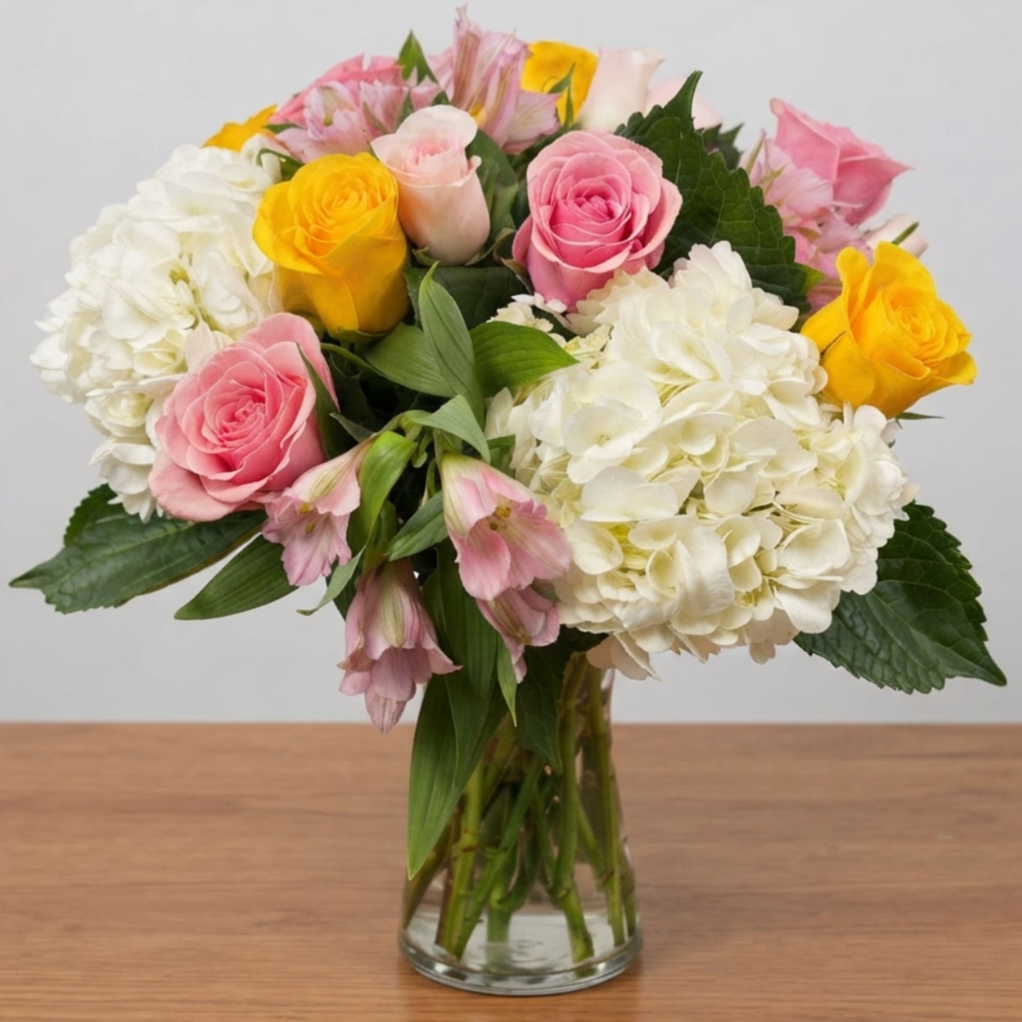 Mixed bouquet of pink and yellow roses with white hydrangeas in a glass vase