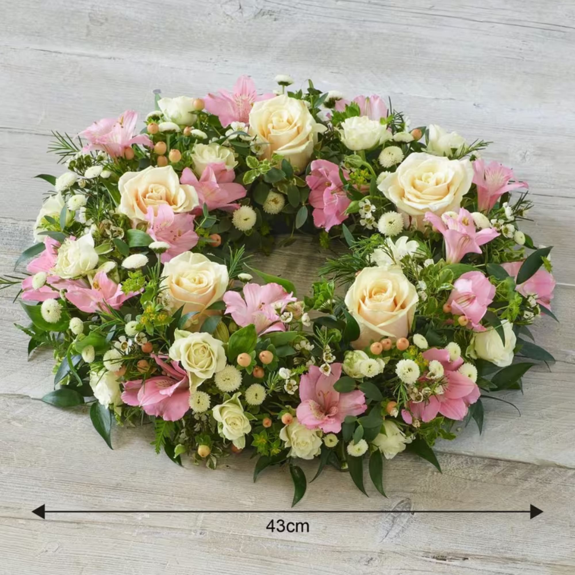 Oval floral wreath with cream roses and pink blooms on a wood background