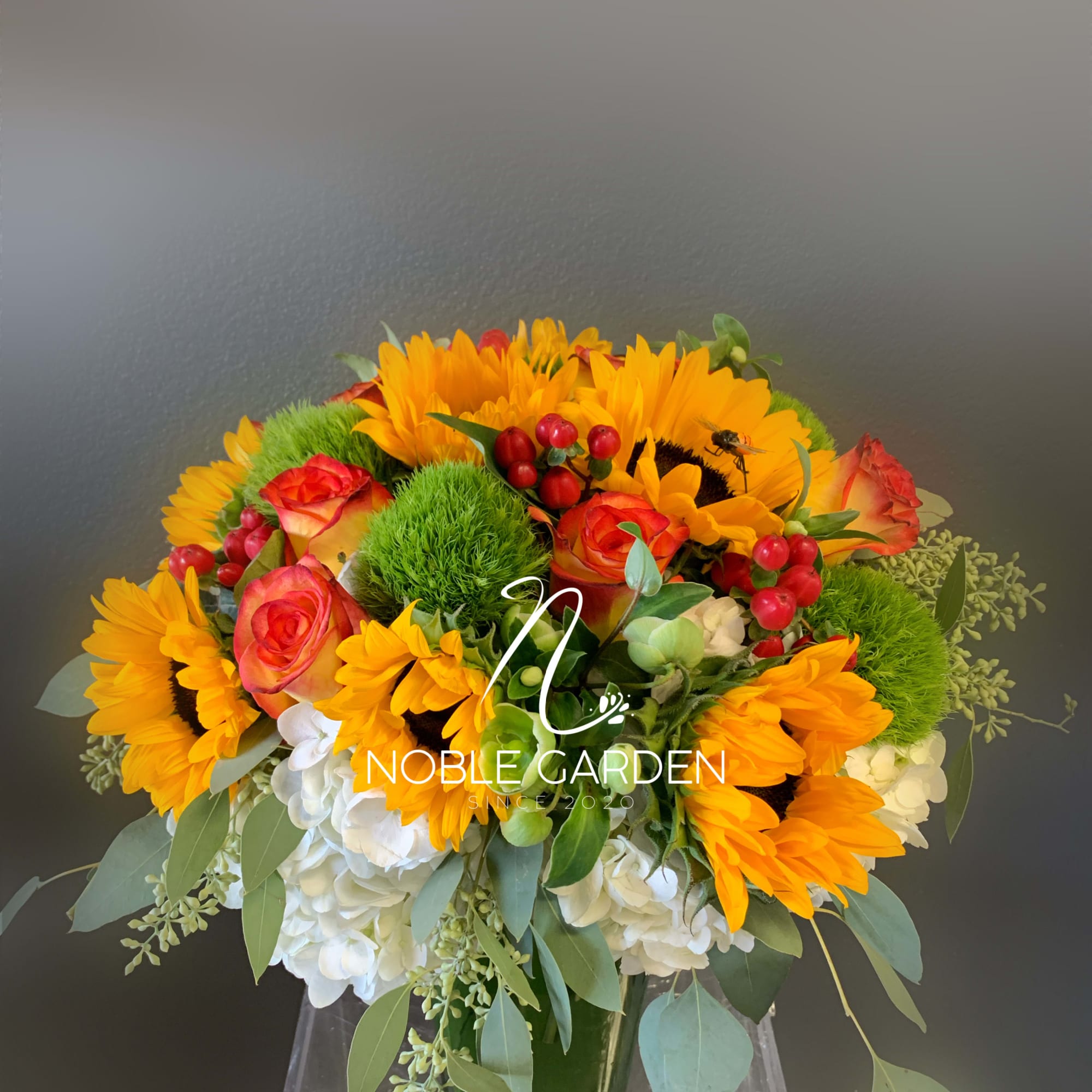 Bouquet of sunflowers, orange roses, and white hydrangeas in a glass vase
