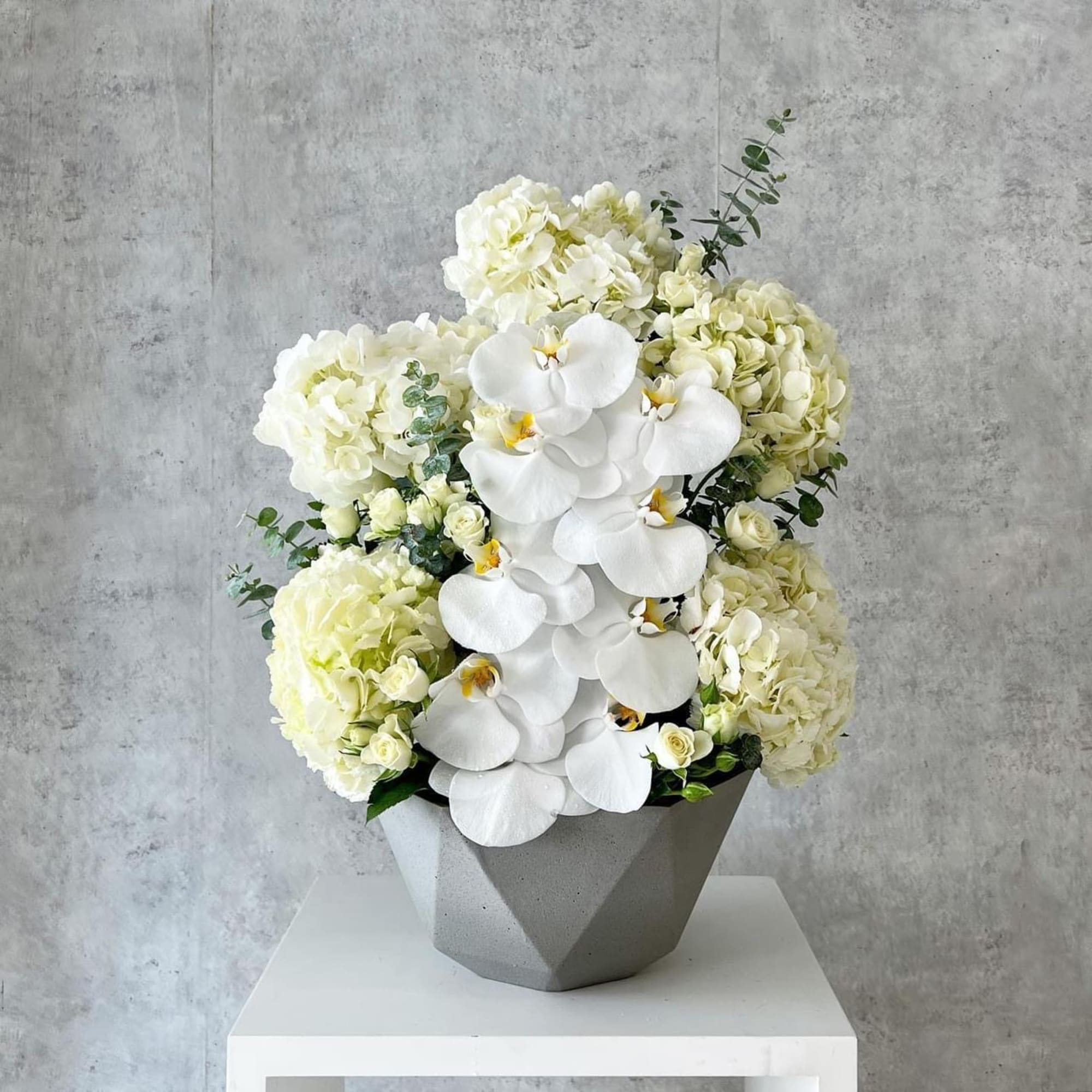 White orchids and pale hydrangeas in a gray geometric vase