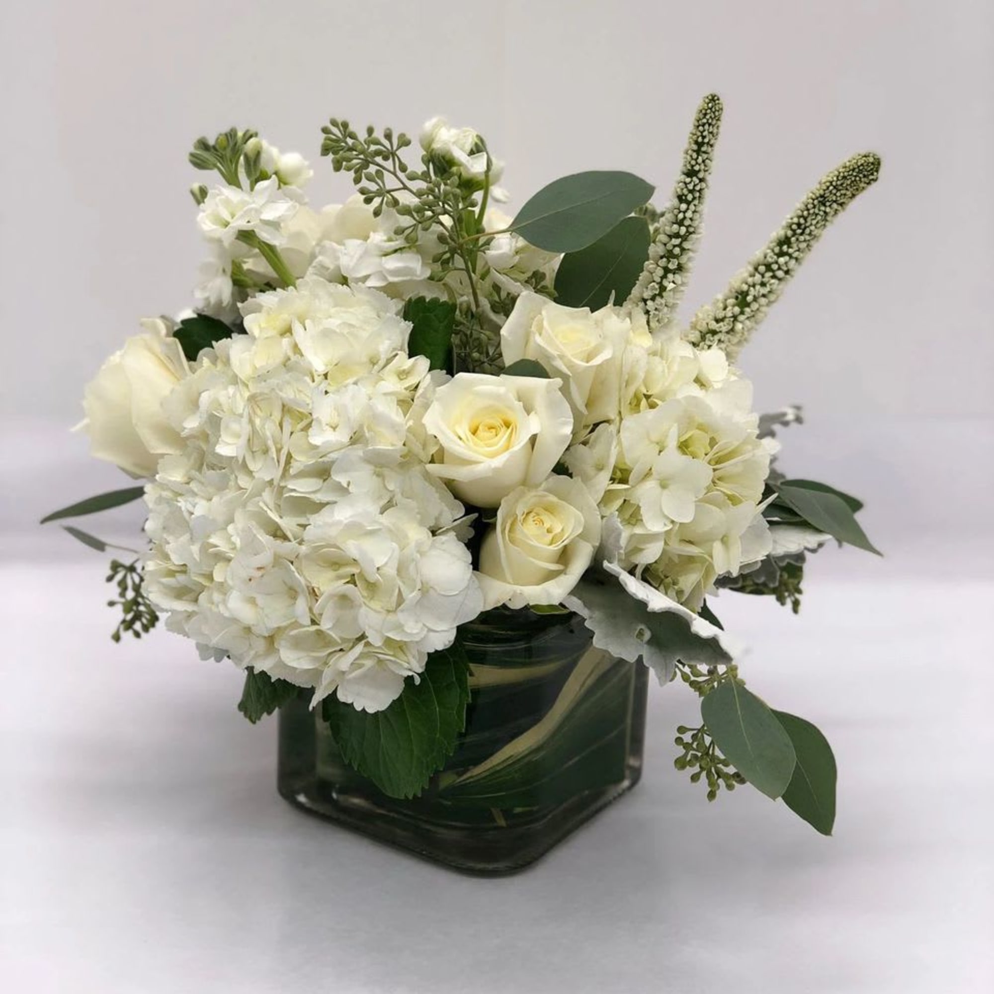 White roses and hydrangeas in a square glass vase