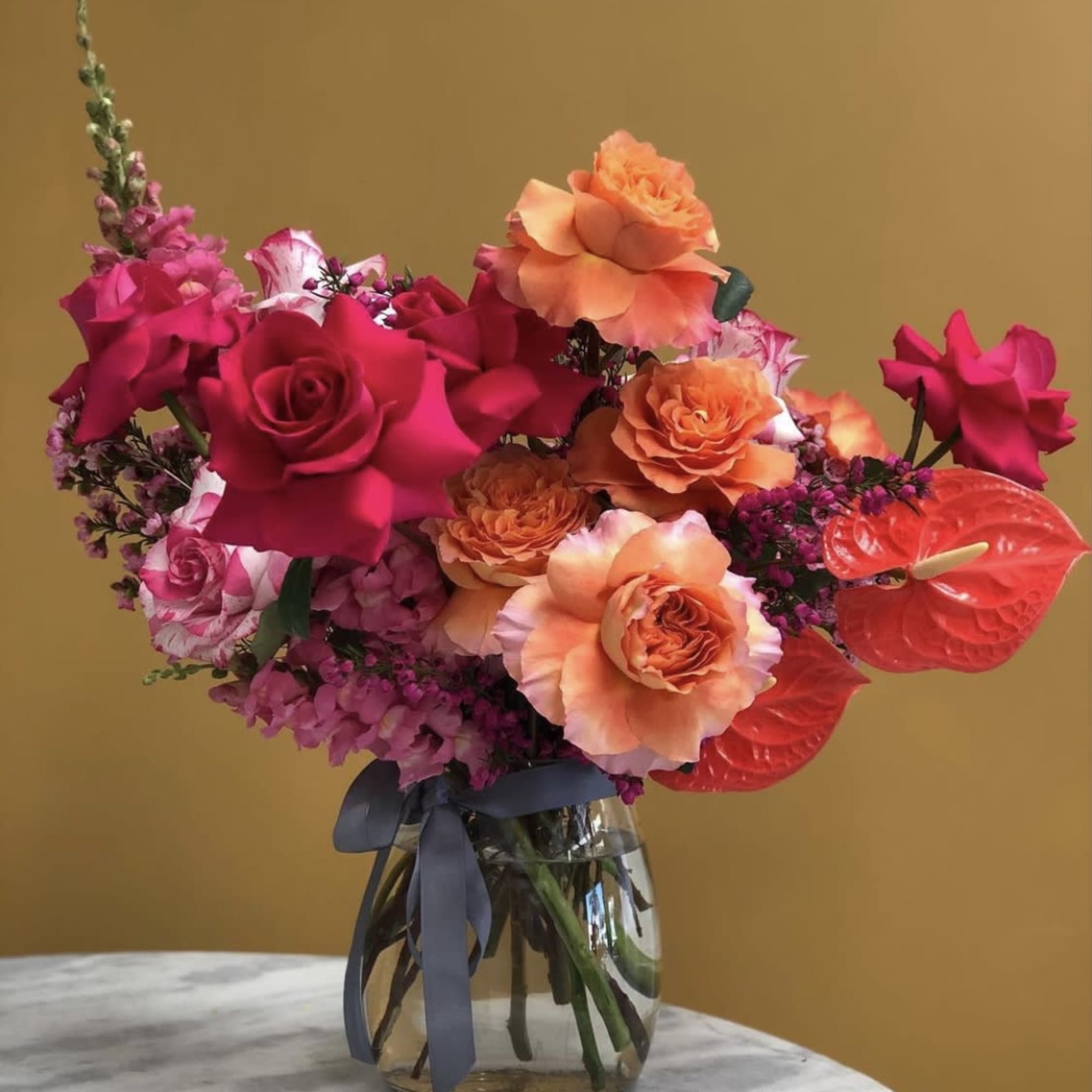 Bright pink and orange rose bouquet in a glass vase with a ribbon