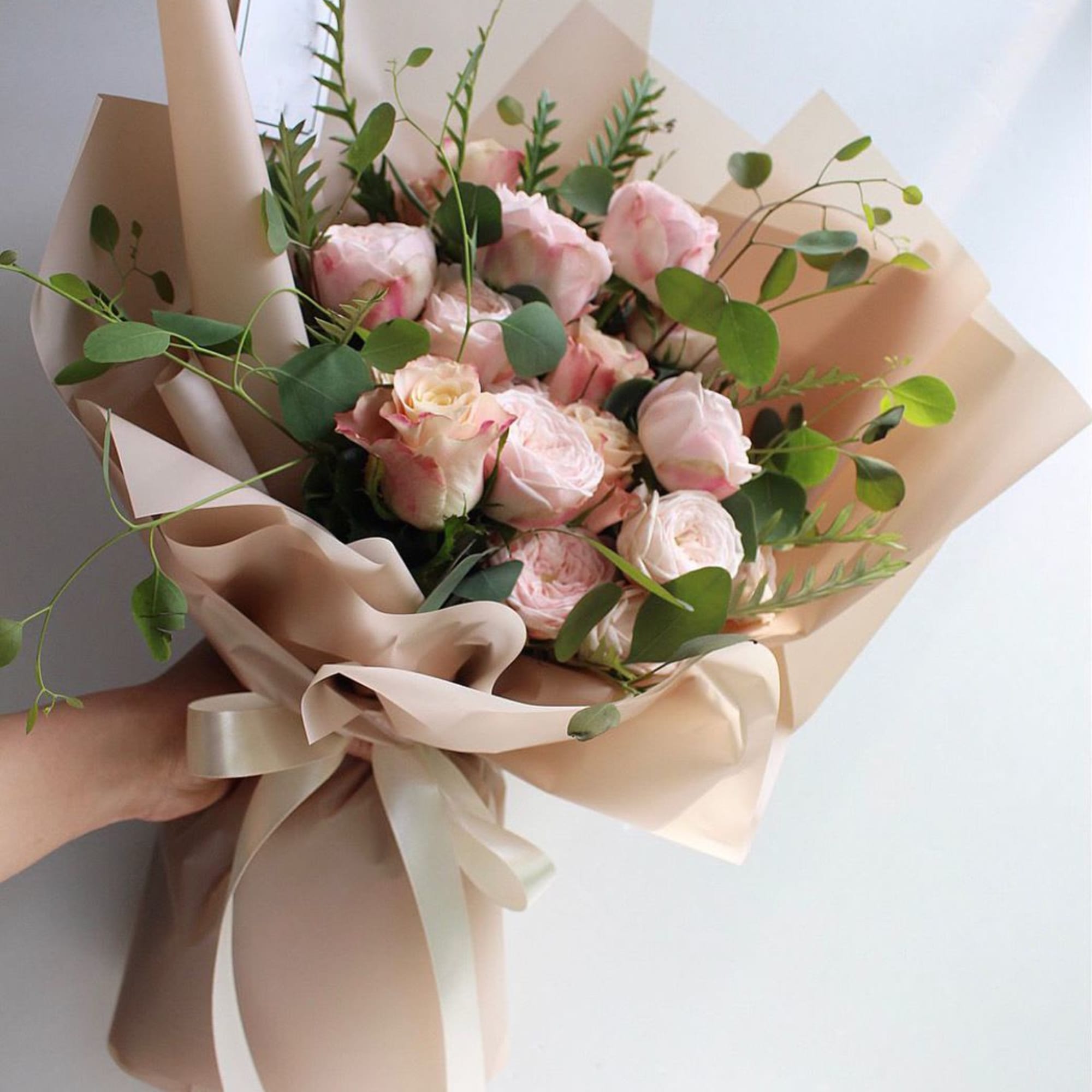 Hand-tied bouquet of pale pink roses with eucalyptus in beige wrap