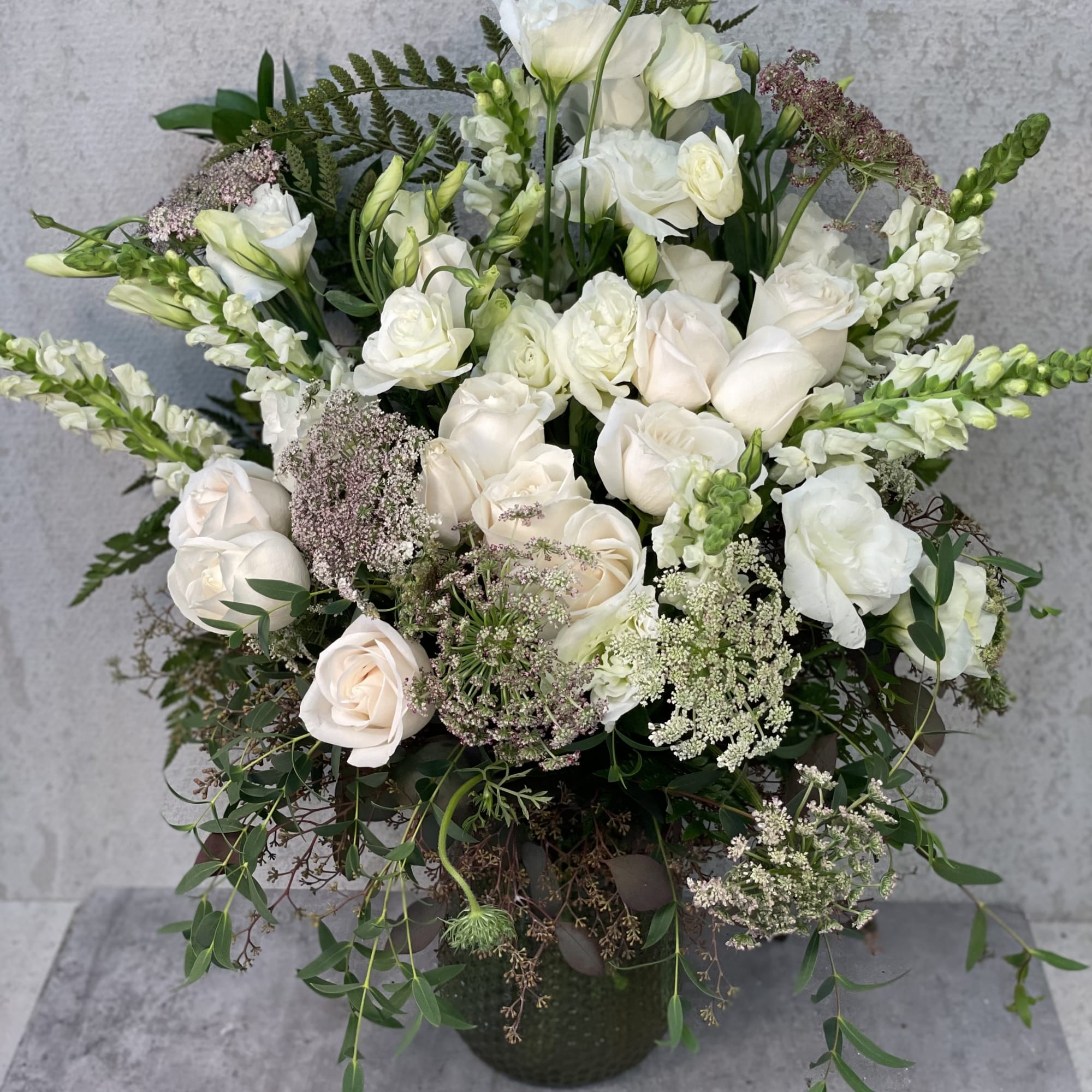 White roses and lisianthus arranged in a dark vase