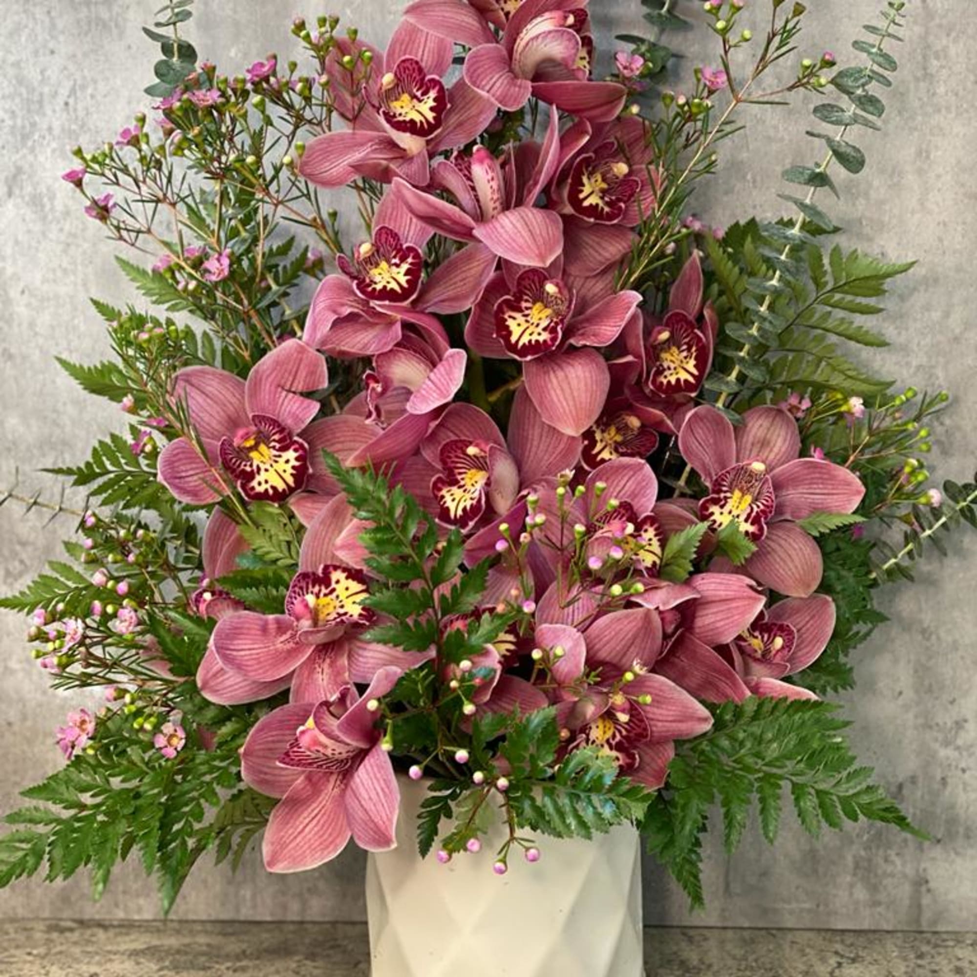 Pink orchid arrangement in a white vase with fern accents