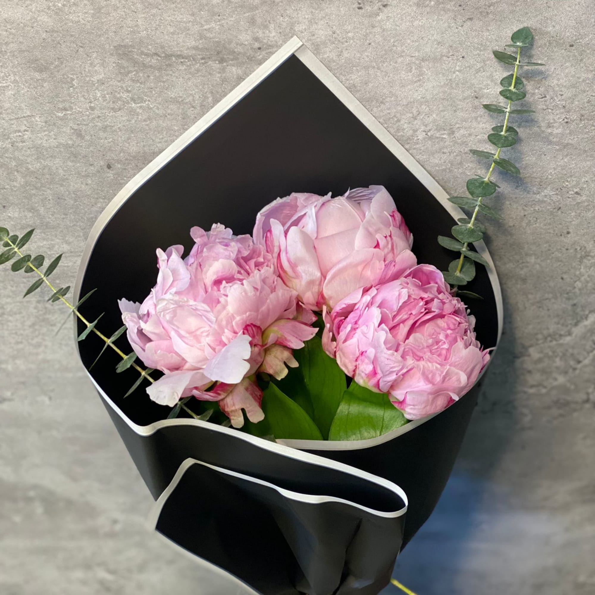 Pink peonies wrapped in black paper with eucalyptus accents