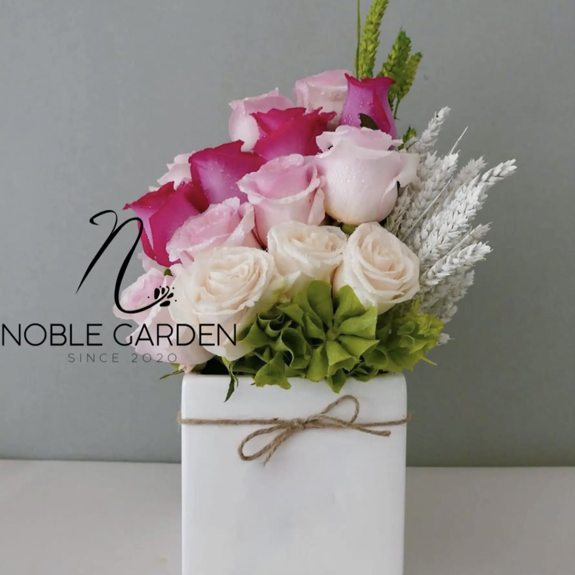 Pink and white roses arranged in a white box with twine