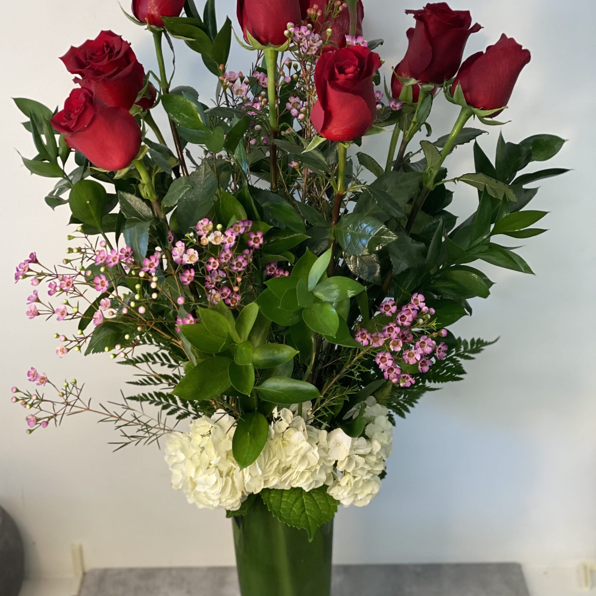 Tall vase arrangement of red roses, pink filler flowers, and white hydrangeas