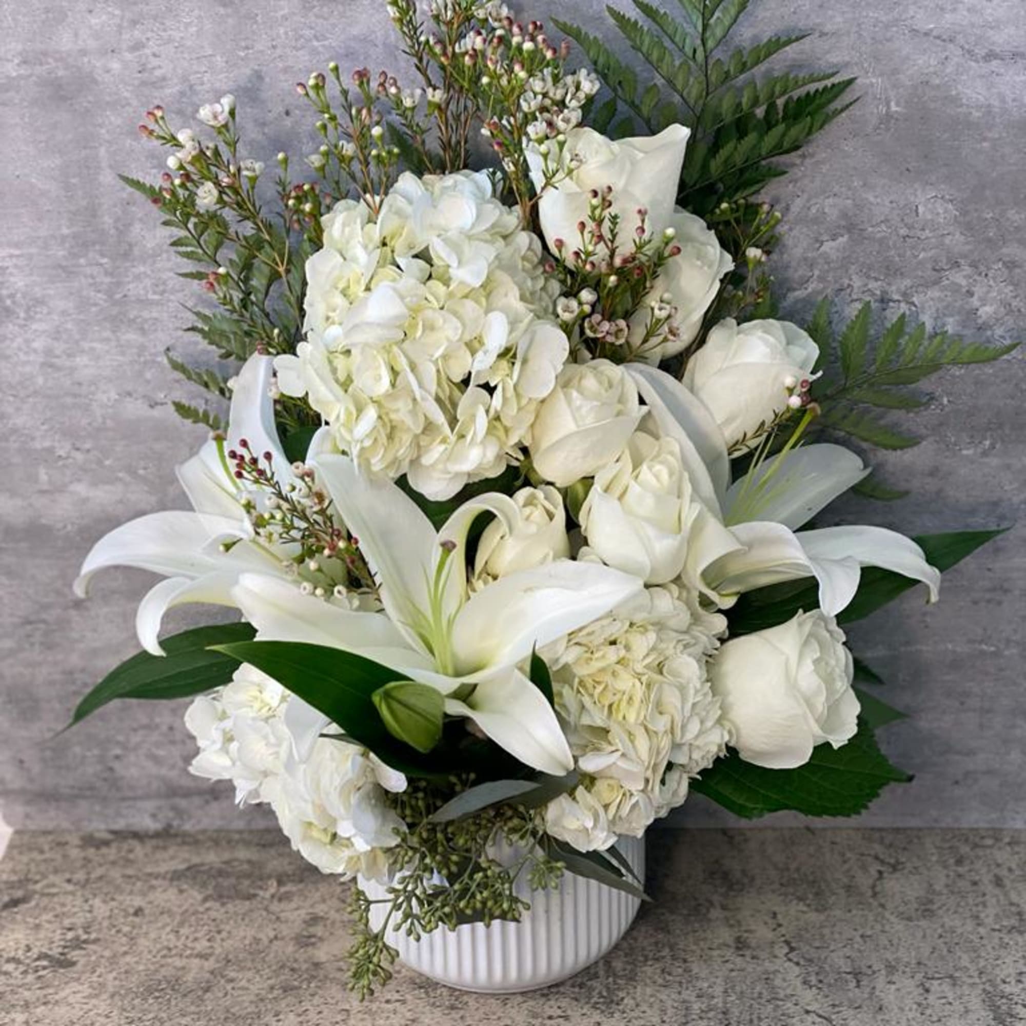 White floral arrangement with lilies, roses, and hydrangeas in a white vase