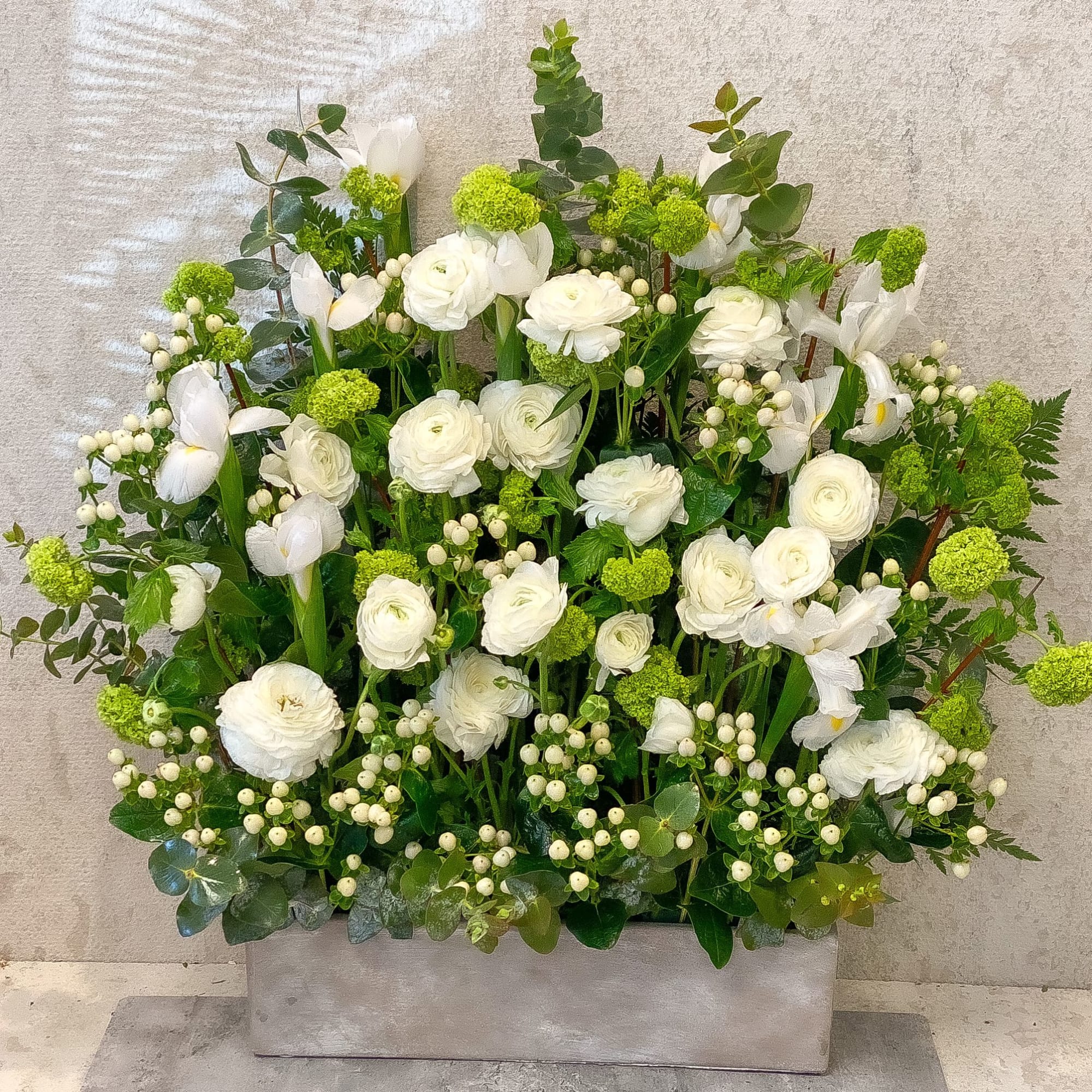 White floral arrangement with green accents in a rectangular container