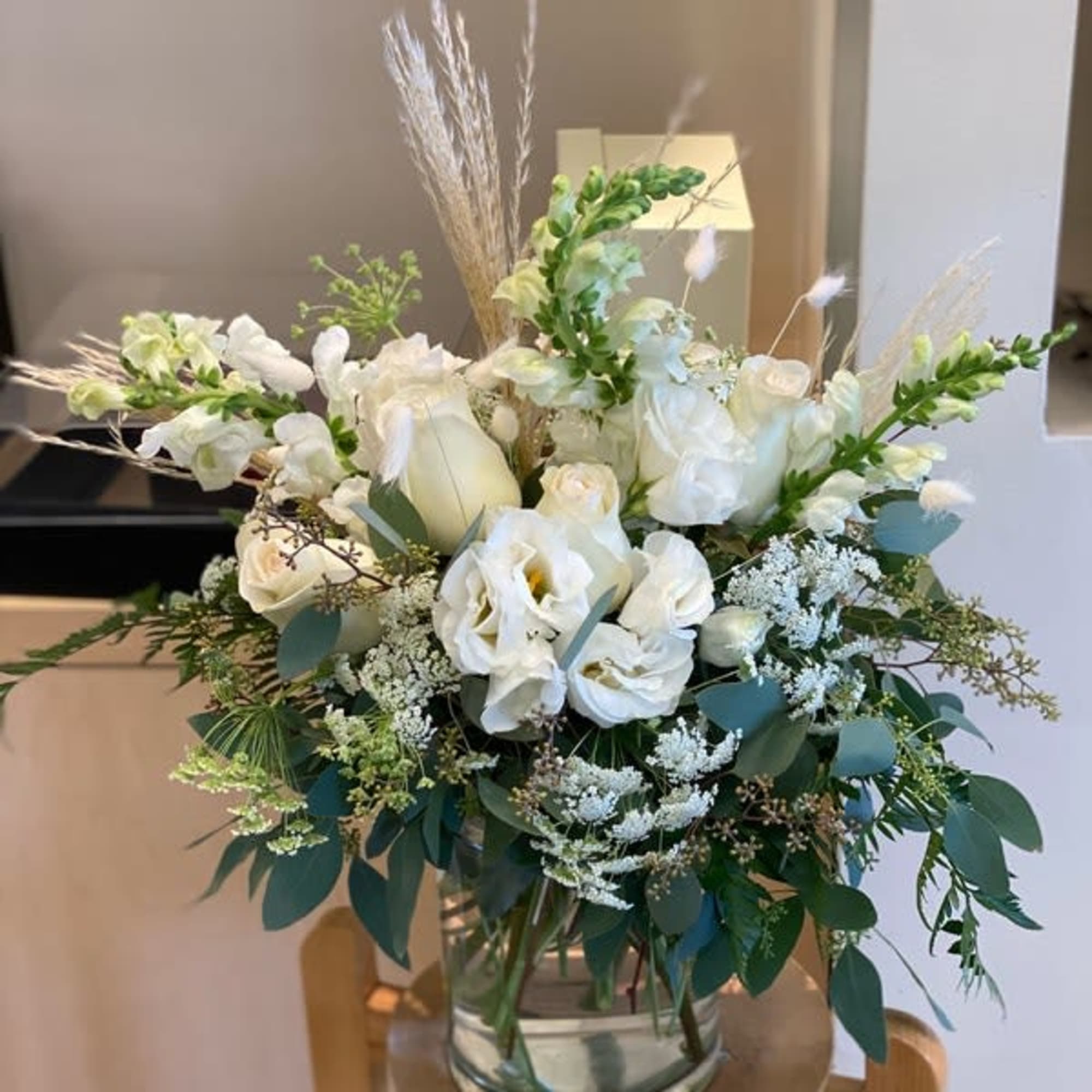 White floral arrangement in a clear glass vase with greenery