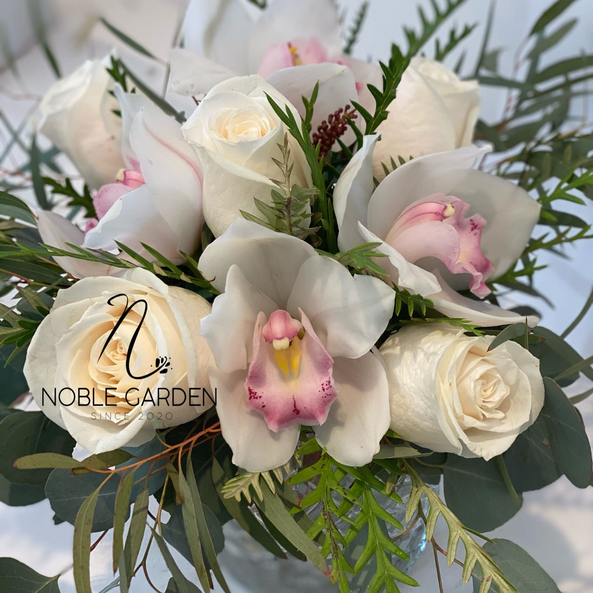 White roses and pink orchids in a bouquet with greenery