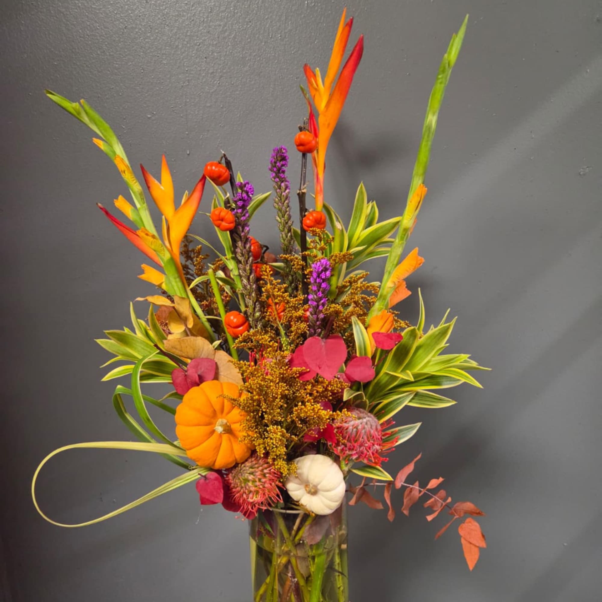 Tall autumn floral arrangement with pumpkins in a glass vase