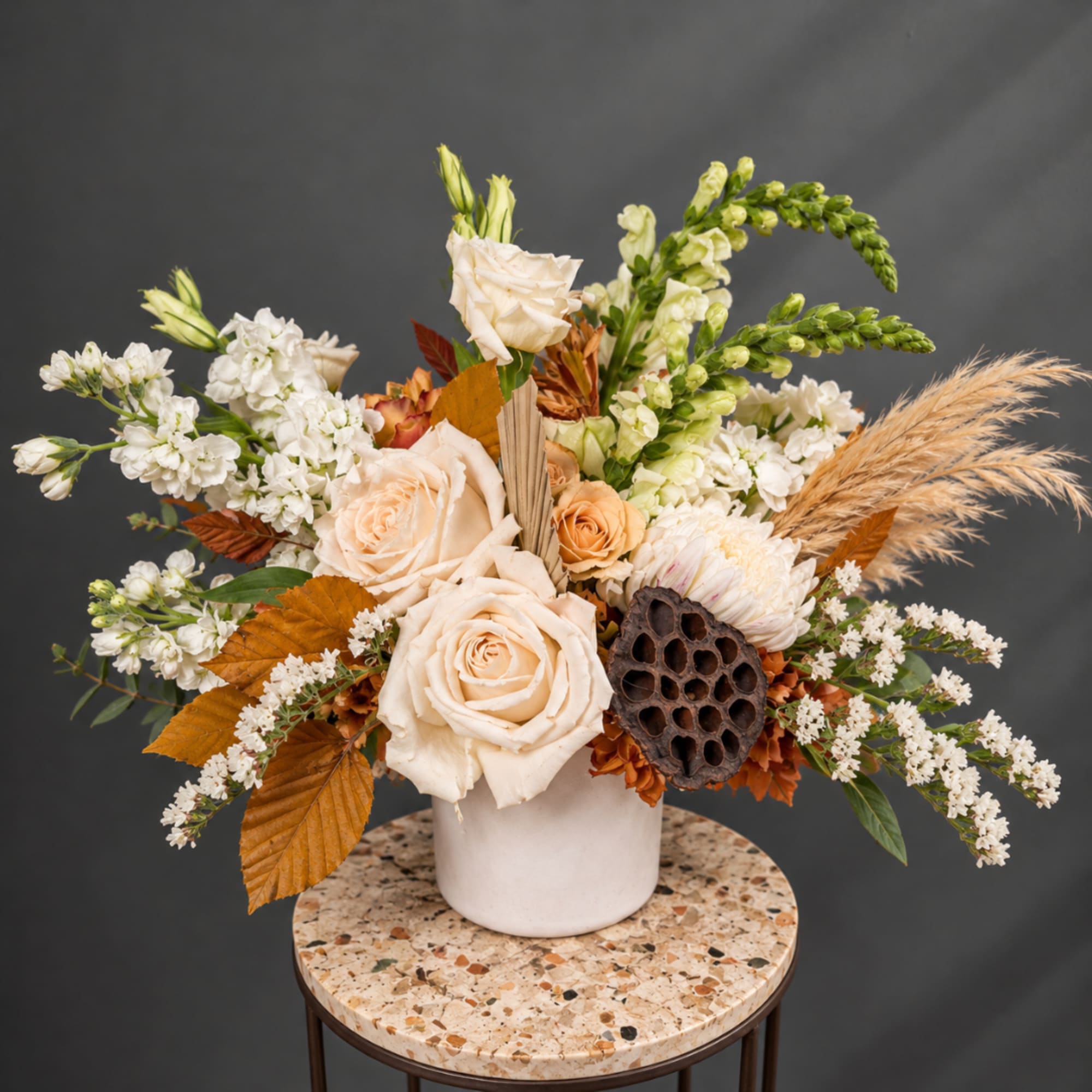 Cream rose arrangement in a white vase with white blooms and dried grasses