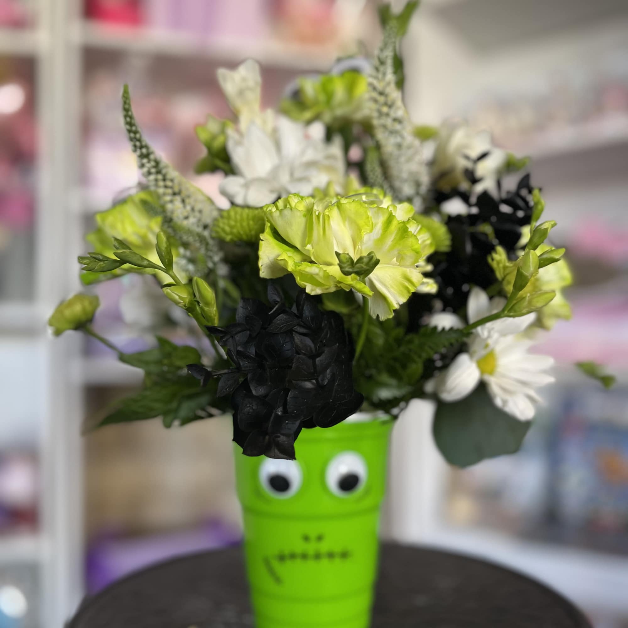Bouquet of green, white, and black flowers in a bright green cup with eyes