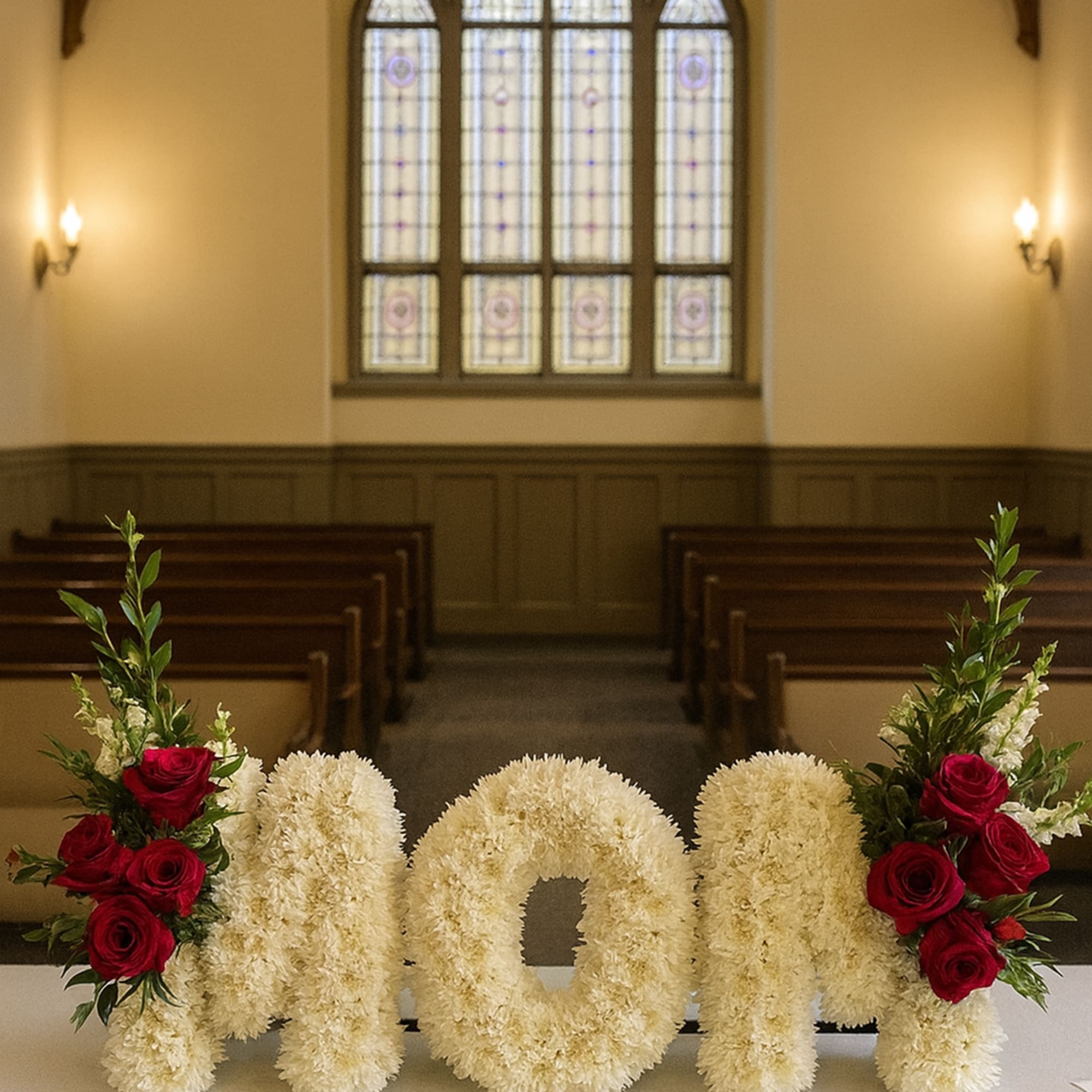 Floral arrangement spelling "mom" with red roses in a church setting