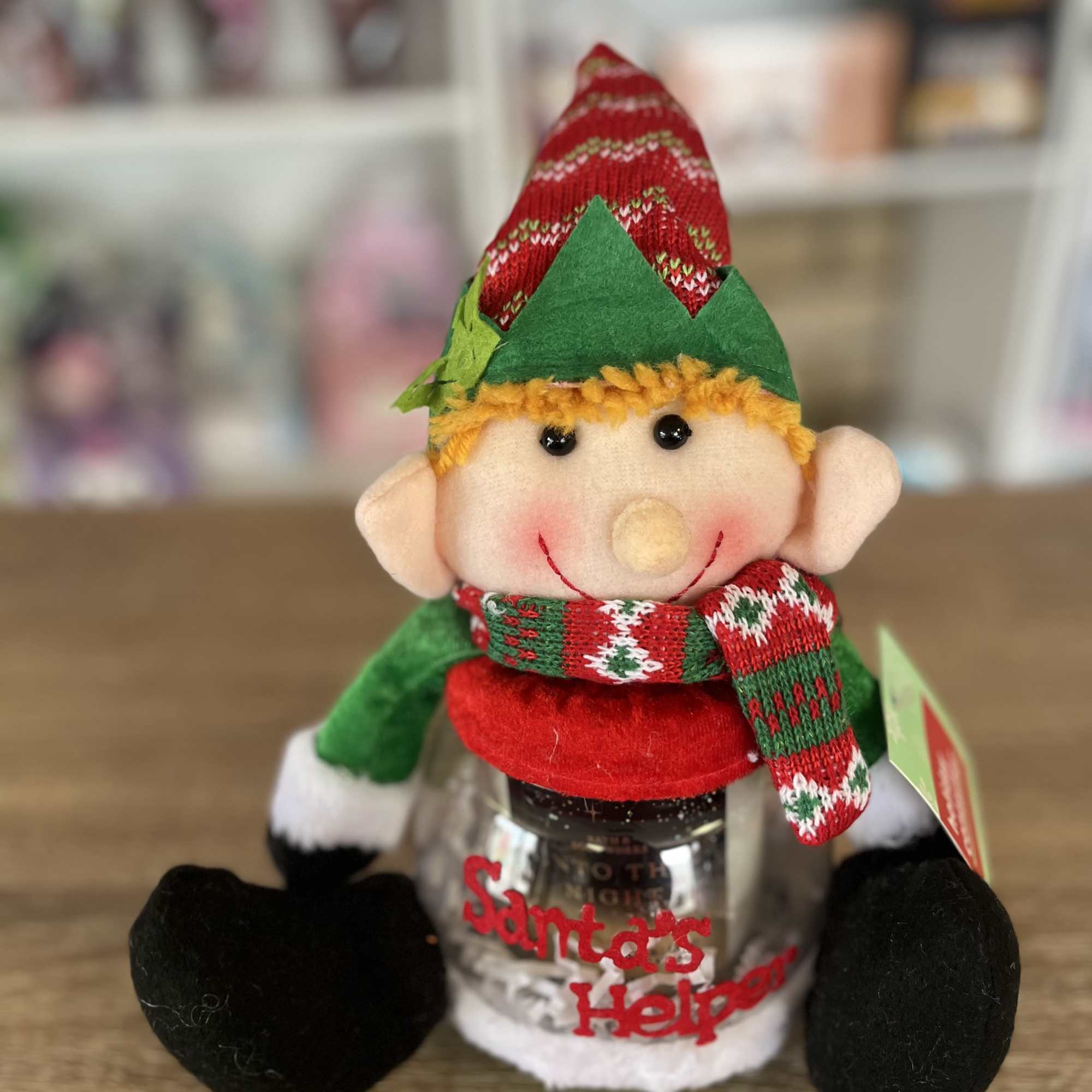 Elf plush sitting on a jar labeled Santa's Helper