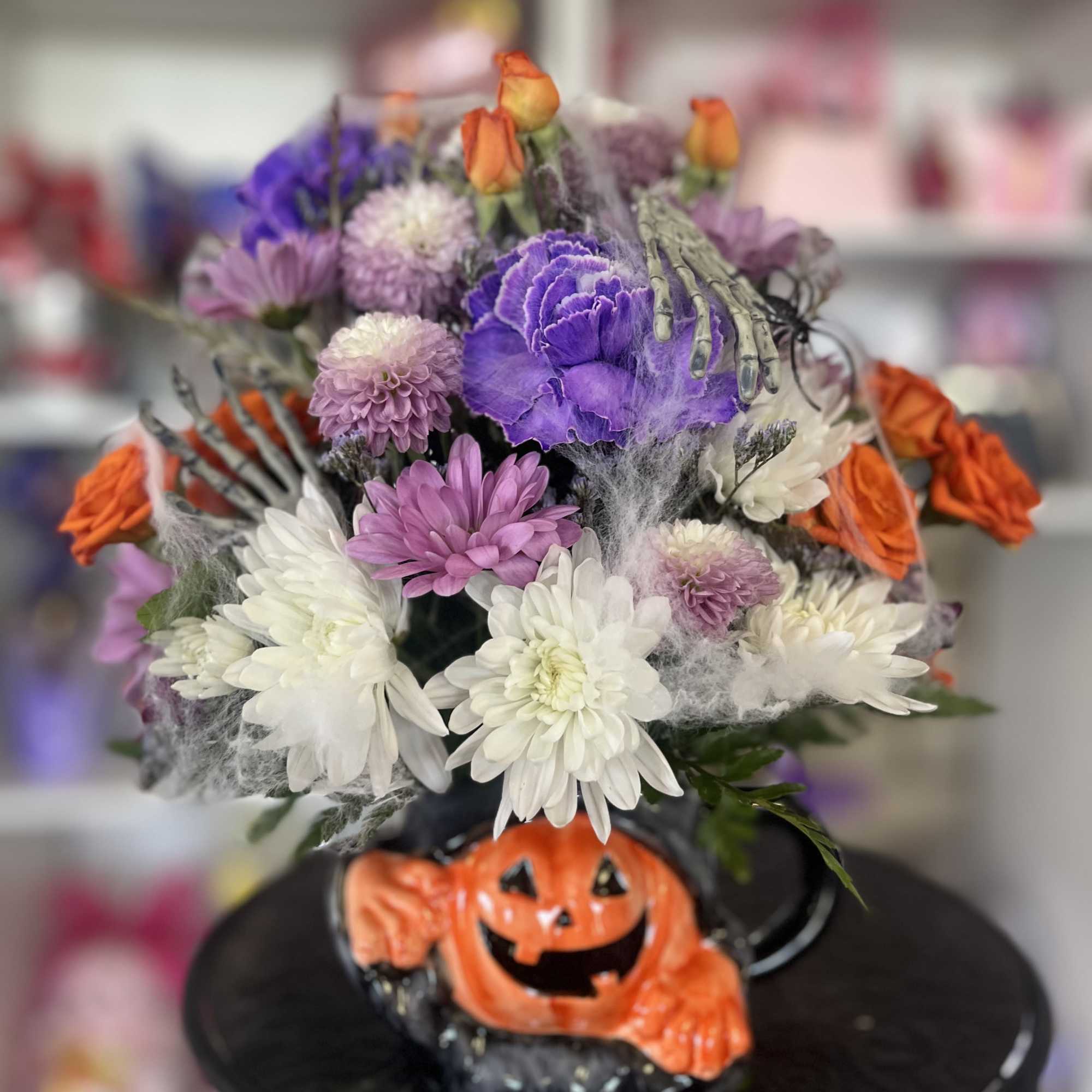 Halloween bouquet with purple, white, and orange flowers in a pumpkin base