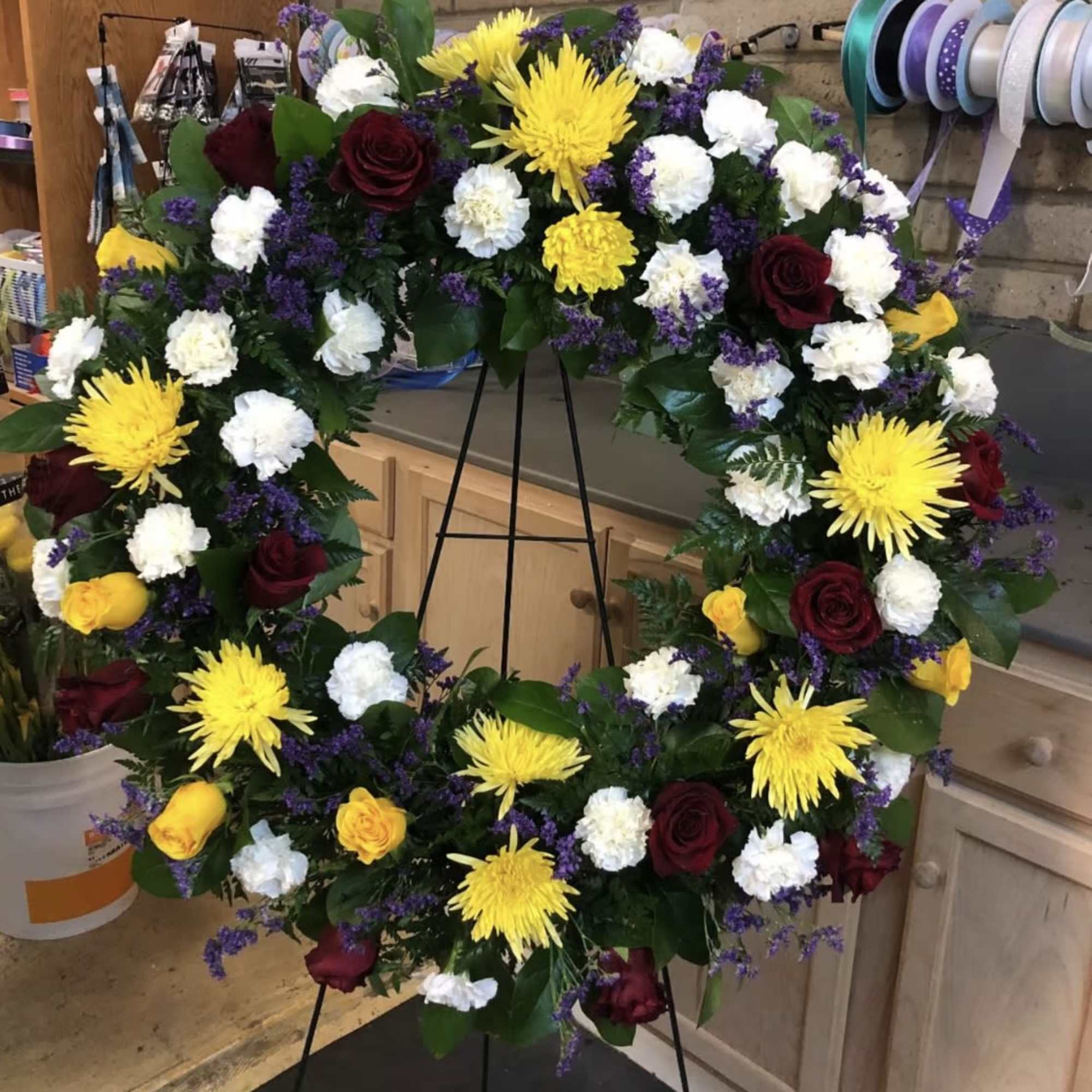 Large floral wreath with yellow, white, purple, and burgundy blooms on a stand