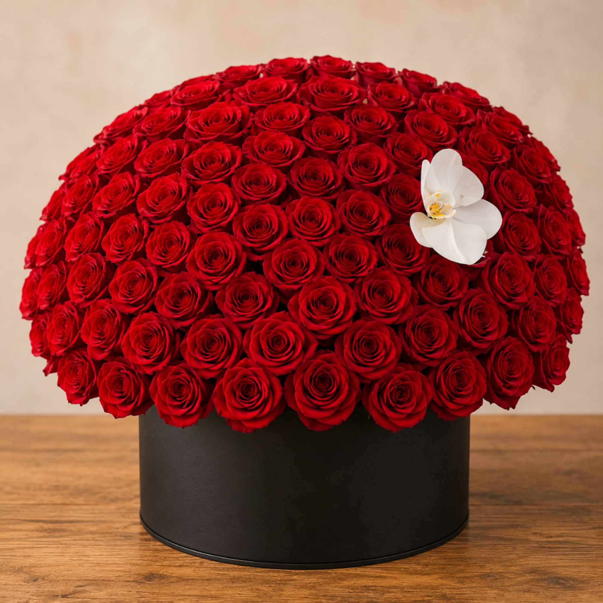 Round arrangement of red roses in a black box with a white orchid accent